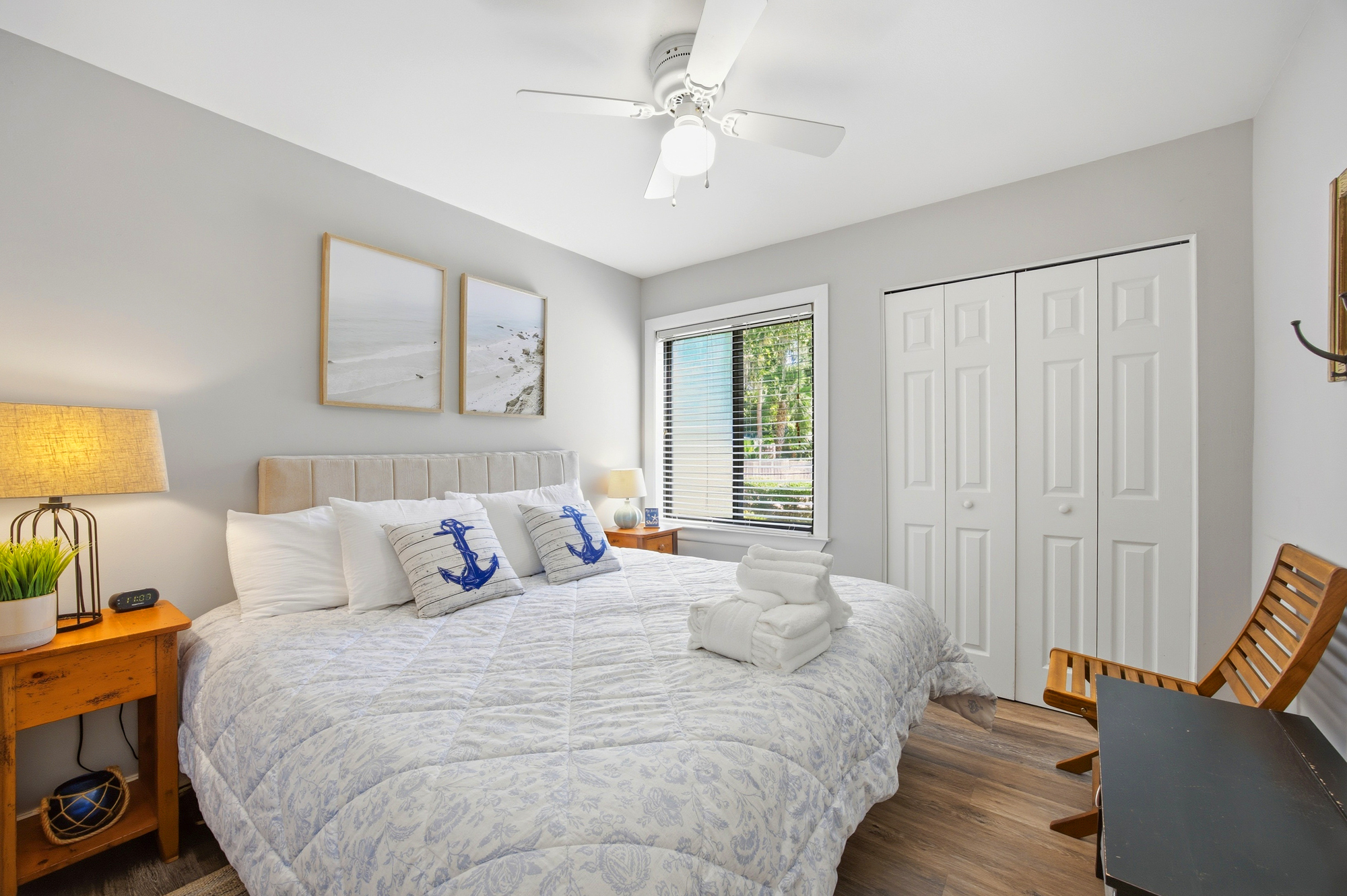 Coastal blue accents and warm wood grain ground this airy bedroom. Afternoon rays filter through the blinds to illuminate the plush linens, while seaside artwork and a gentle ceiling fan create a peaceful atmosphere for your rest.