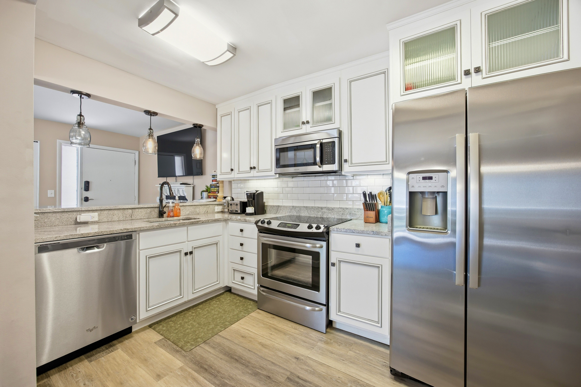White cabinetry and glass-front doors bring a sense of airy openness to this modern chef's corner. Speckled counters and brushed metal appliances create a sleek yet warm space for preparing morning coffee or a quiet dinner at home.