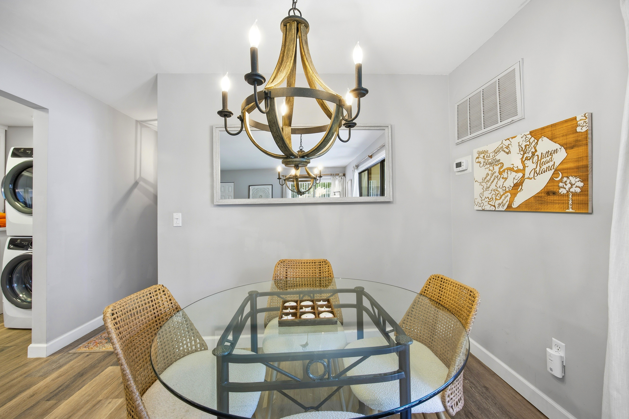 Warm wood accents and a rustic wagon wheel chandelier anchor this intimate dining nook. Rattan chairs and a glass tabletop create an airy, seaside feel, perfect for sharing a peaceful morning meal or planning the day's island adventures.