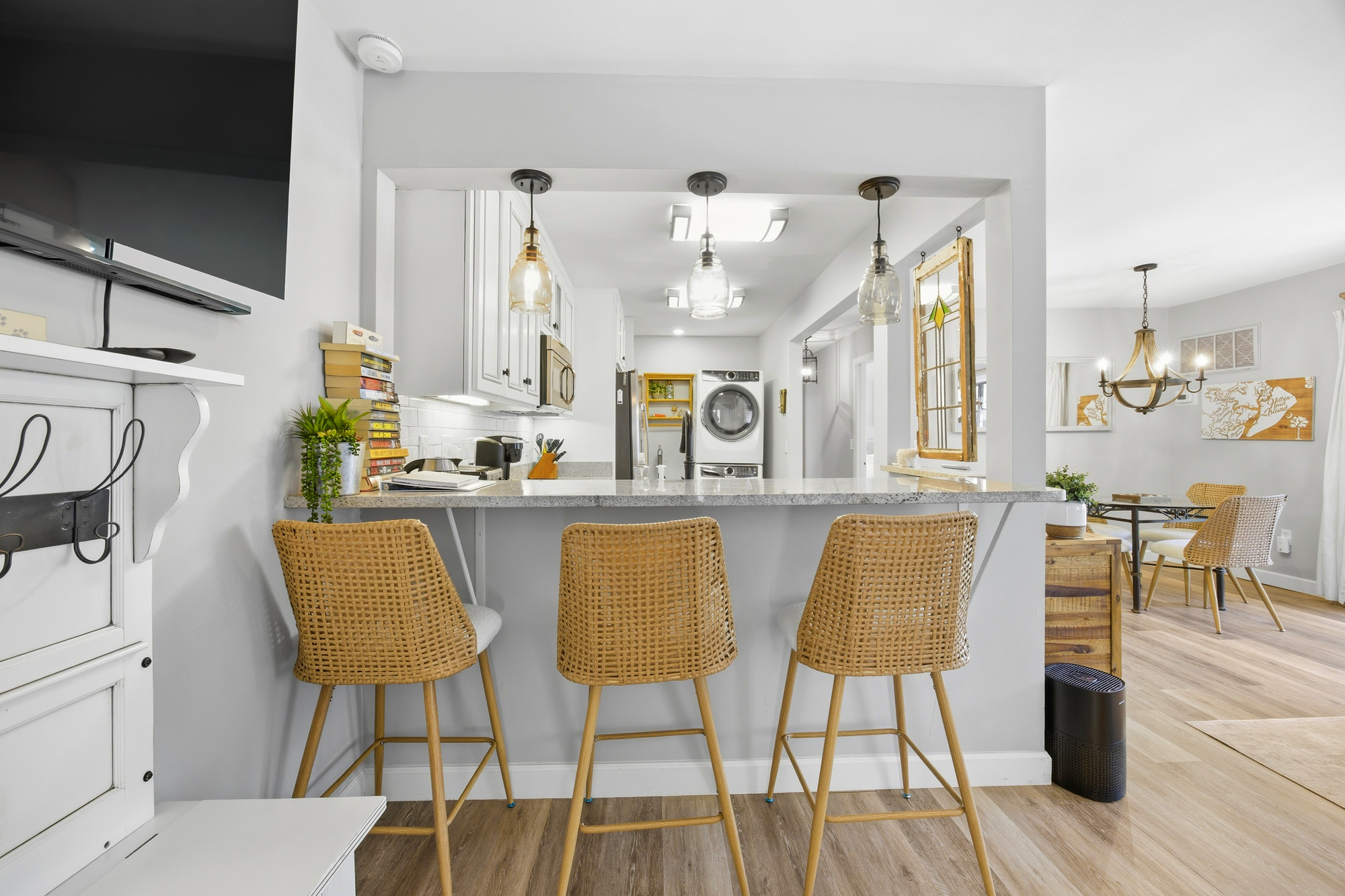 Morning light glows through glass pendants, illuminating the speckled counters and textured barstools. This open kitchen invites slow breakfasts and easy conversation across the airy, sun-drenched space.