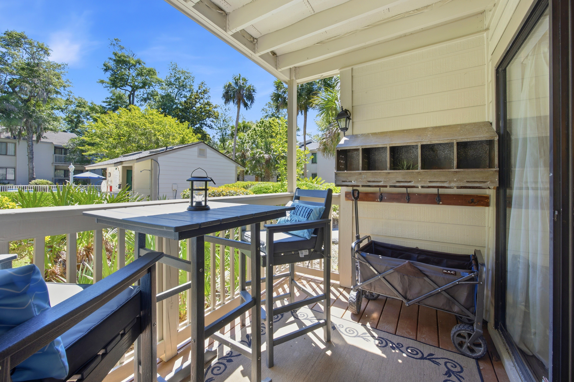 Dark wood bistro seating offers a quiet spot to survey the lush greenery and palm trees under a bright sky. Rustic accents and comfortable cushions create a cozy nook for your coffee on this shaded, private balcony.
