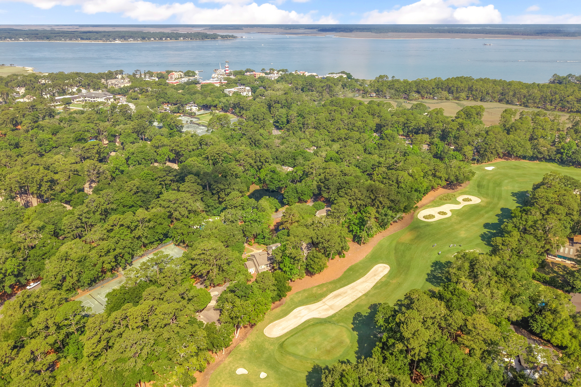 Coastal pines and manicured fairways meet the sparkling blue of the Sound in this expansive aerial vista. Afternoon glow illuminates the dense canopy and sandy bunkers, offering a glimpse of the island's scenic landscape above this distinct villa!