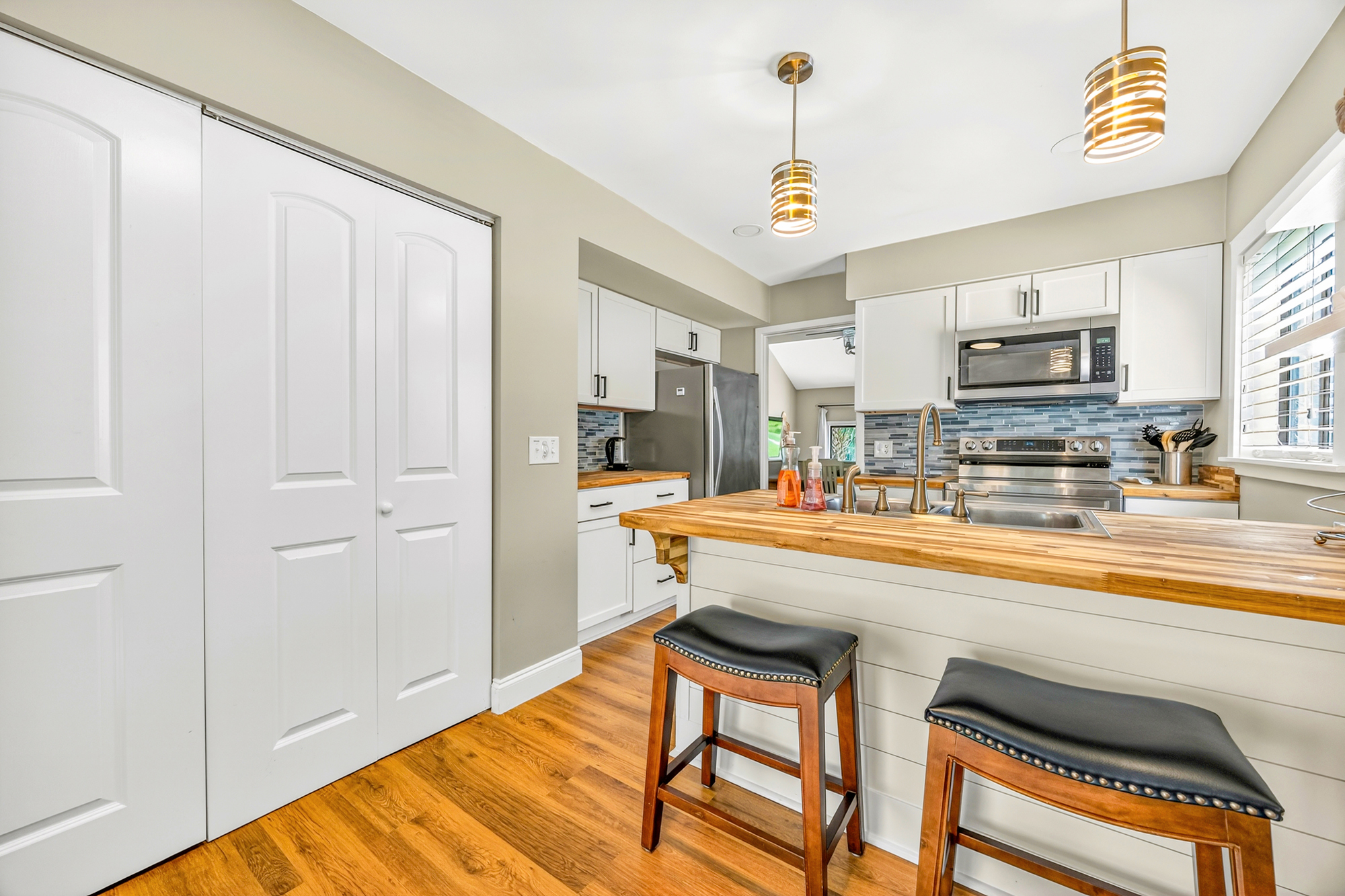 Butcher block countertops and warm wood floors anchor this bright kitchen, where gold pendant lights cast a soft glow over the breakfast bar. Slate blue tiles add a modern touch to the airy space, creating a perfect spot for slow morning coffee.