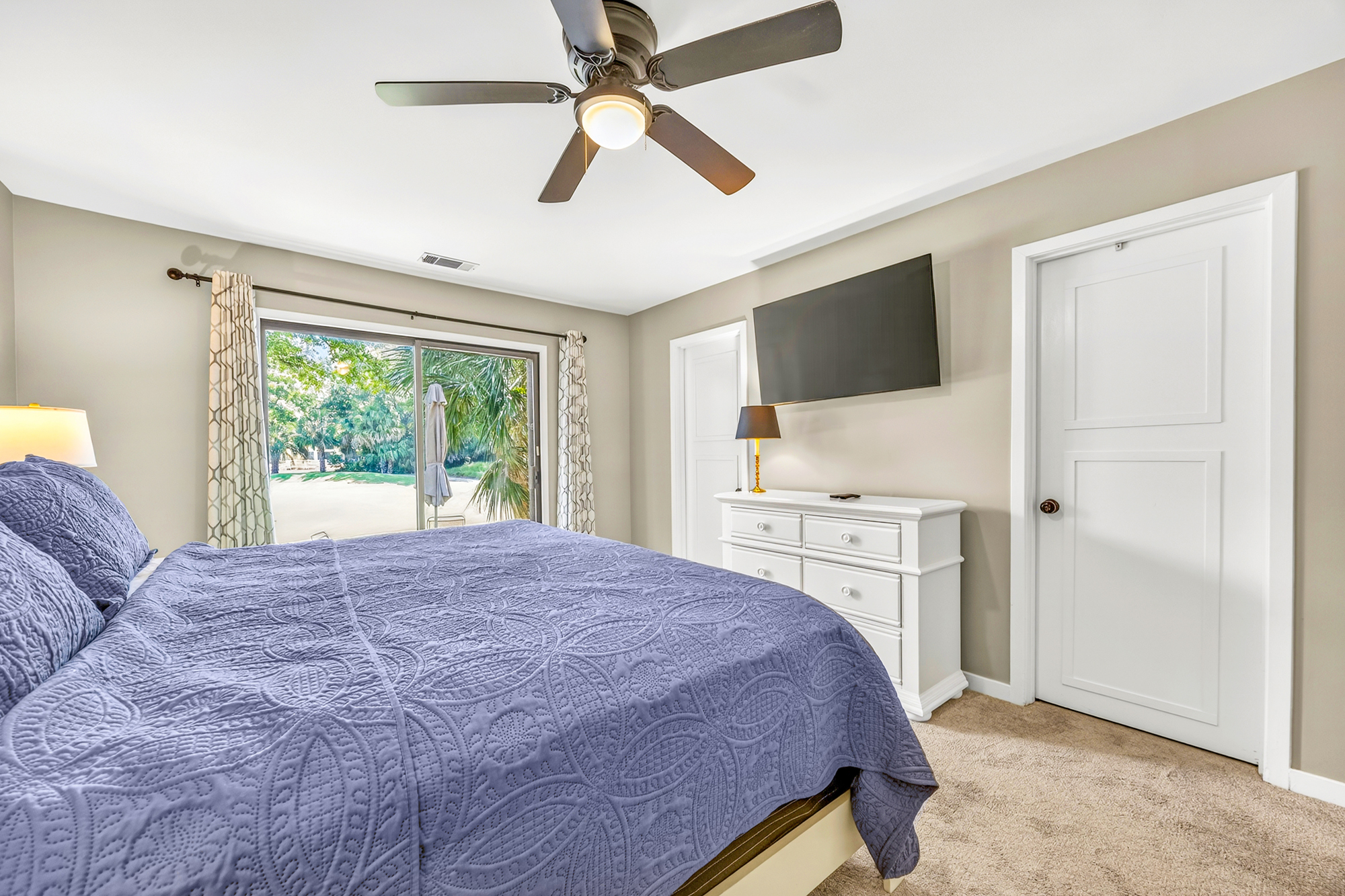 Indigo textures and soft linens ground this airy bedroom, where sliding doors reveal a lush garden view. Warm morning glow fills the space, highlighting the crisp white finishes and plush carpet for a serene start to your day.