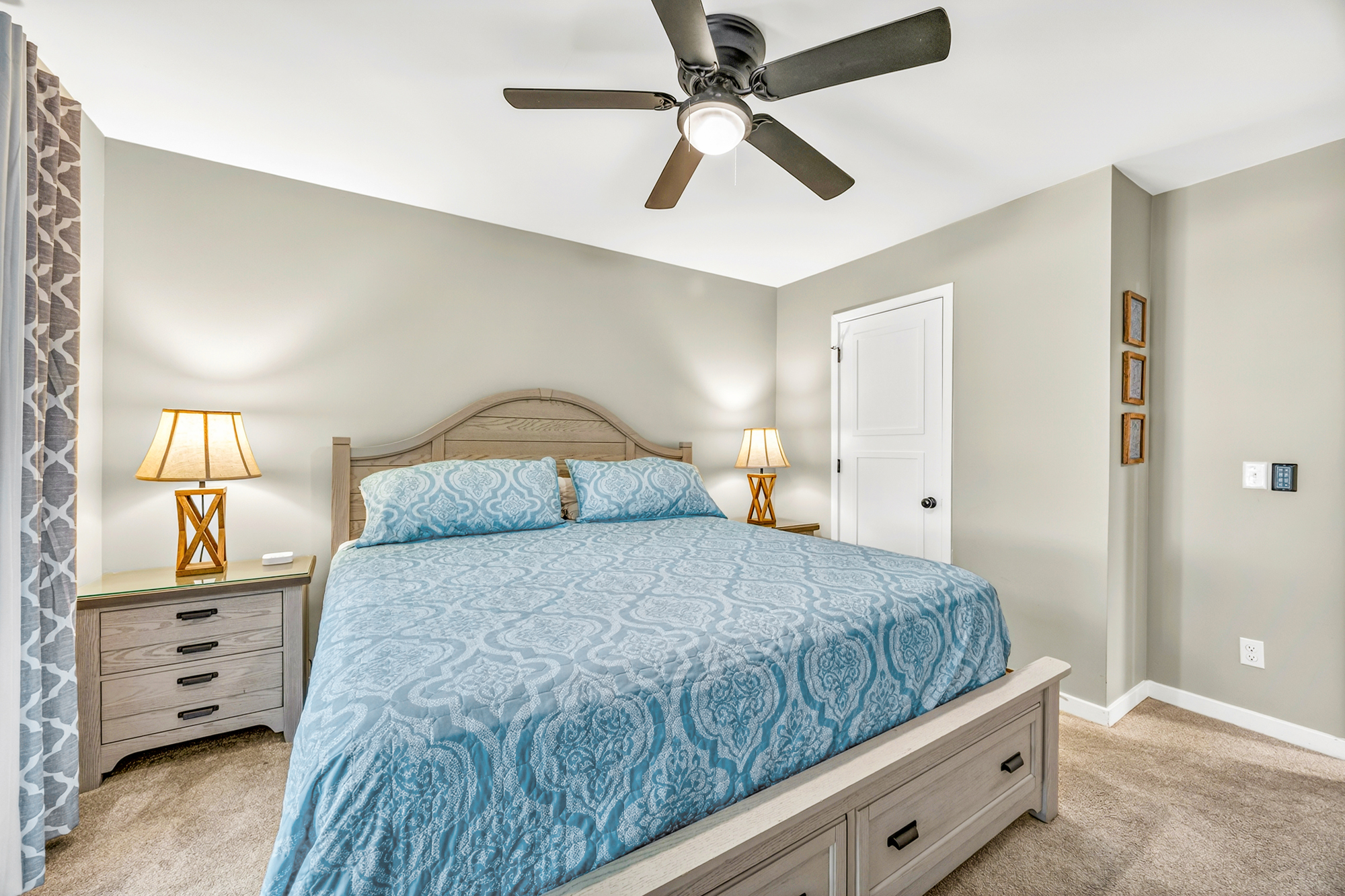 Cerulean patterns dance across the plush bedding, illuminated by the golden radiance of bedside lamps. This serene corner pairs smooth timber textures with cool, quiet tones to create a stationary space for restorative rest.