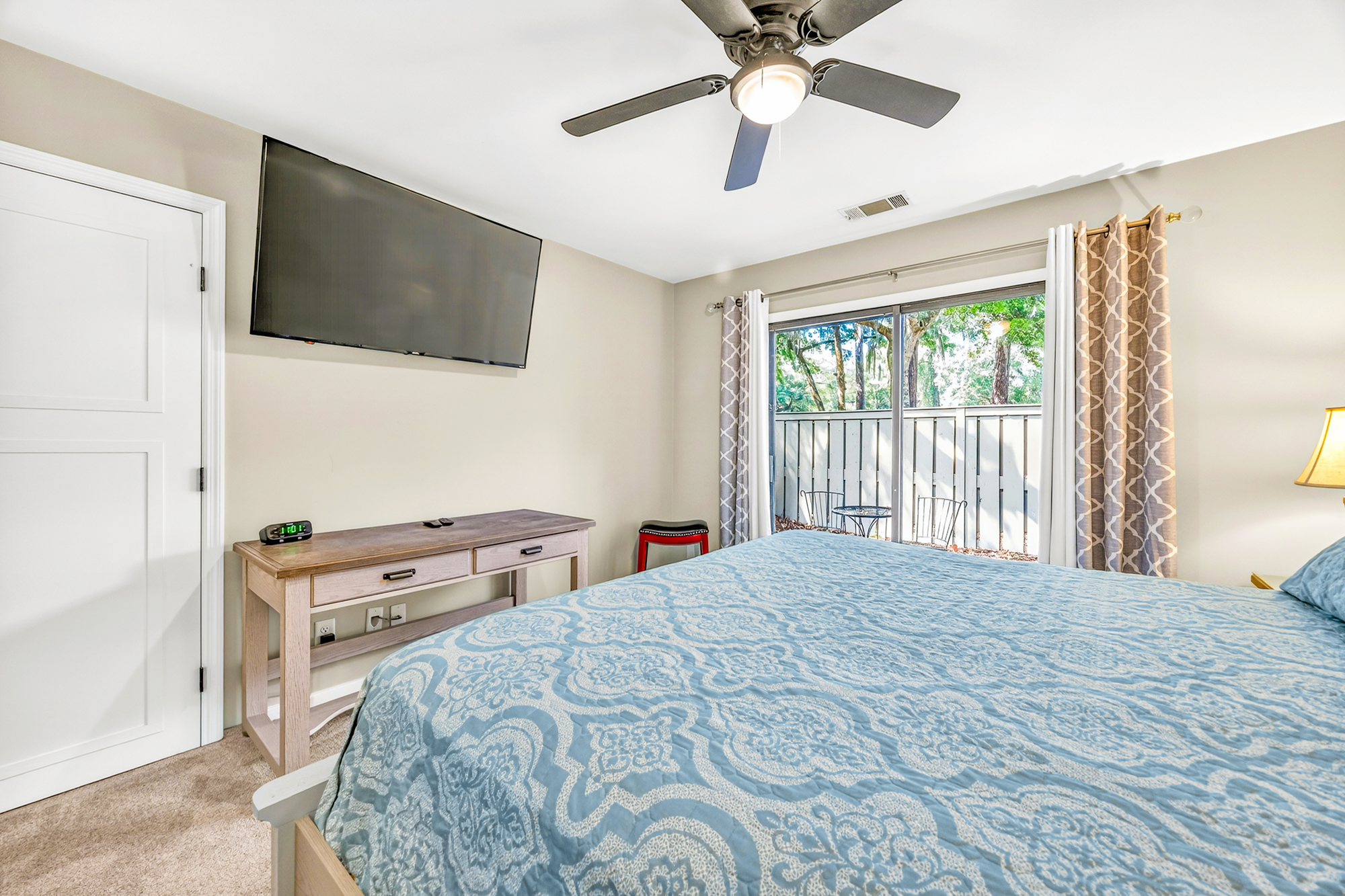 Intricate blue patterns on the quilt pop against neutral walls, while sliding glass doors pull in a lush view of the private patio. Clean lines and a quiet atmosphere make this bedroom a peaceful spot for a movie night or a slow morning.