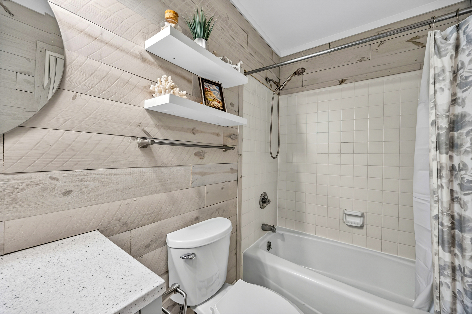 Weathered wood planks bring a coastal texture to this bright bathroom, creating a spa-like atmosphere for your morning routine. Clean white tiles and floating shelves offer a fresh, modern look and plenty of space to prepare for the day.