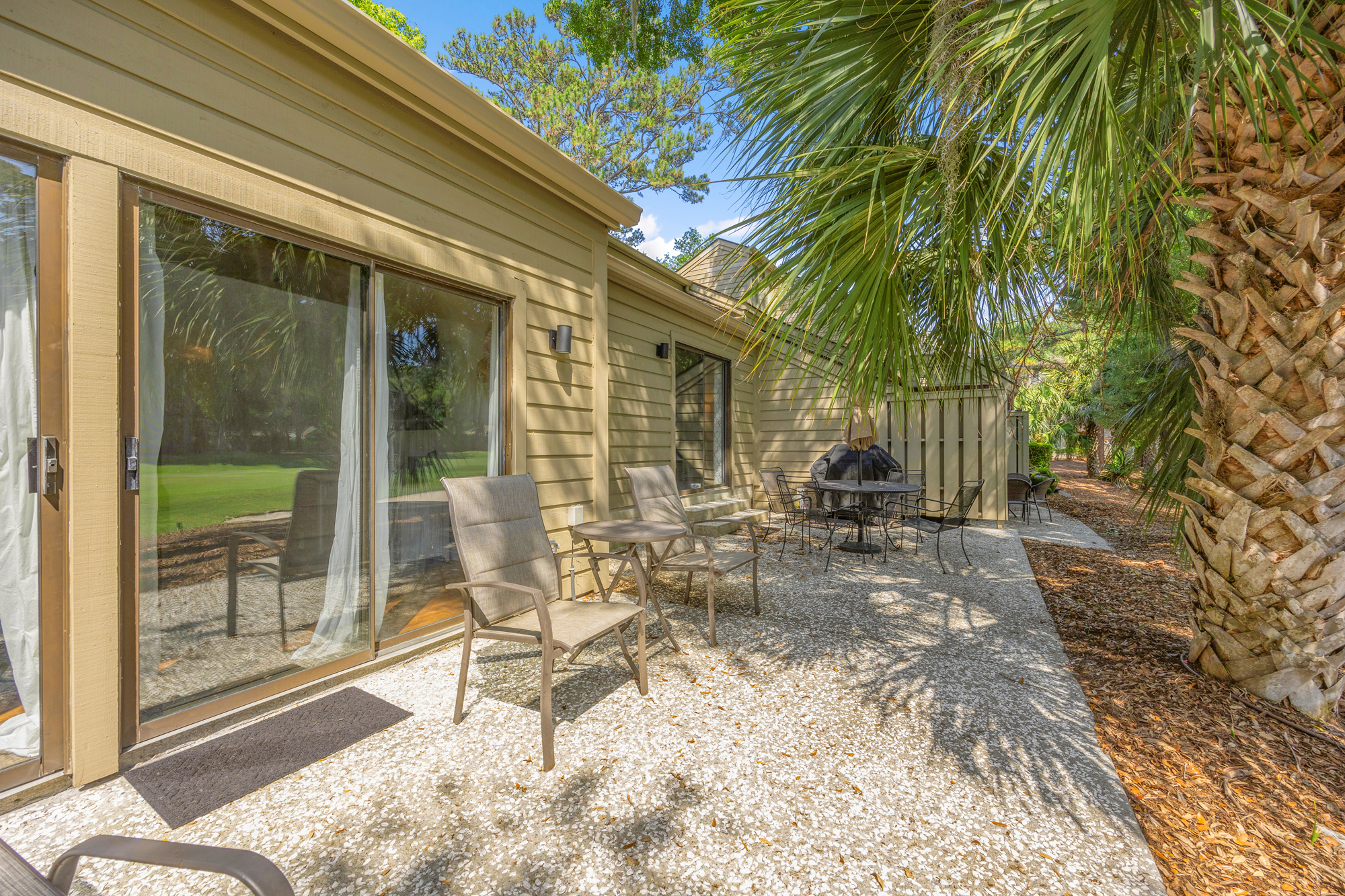 Dappled shadows from swaying palms dance across this private stone patio. Comfortable seating and large glass sliders create a seamless flow between the airy interior and the quiet, leaf-fringed outdoor lounge.