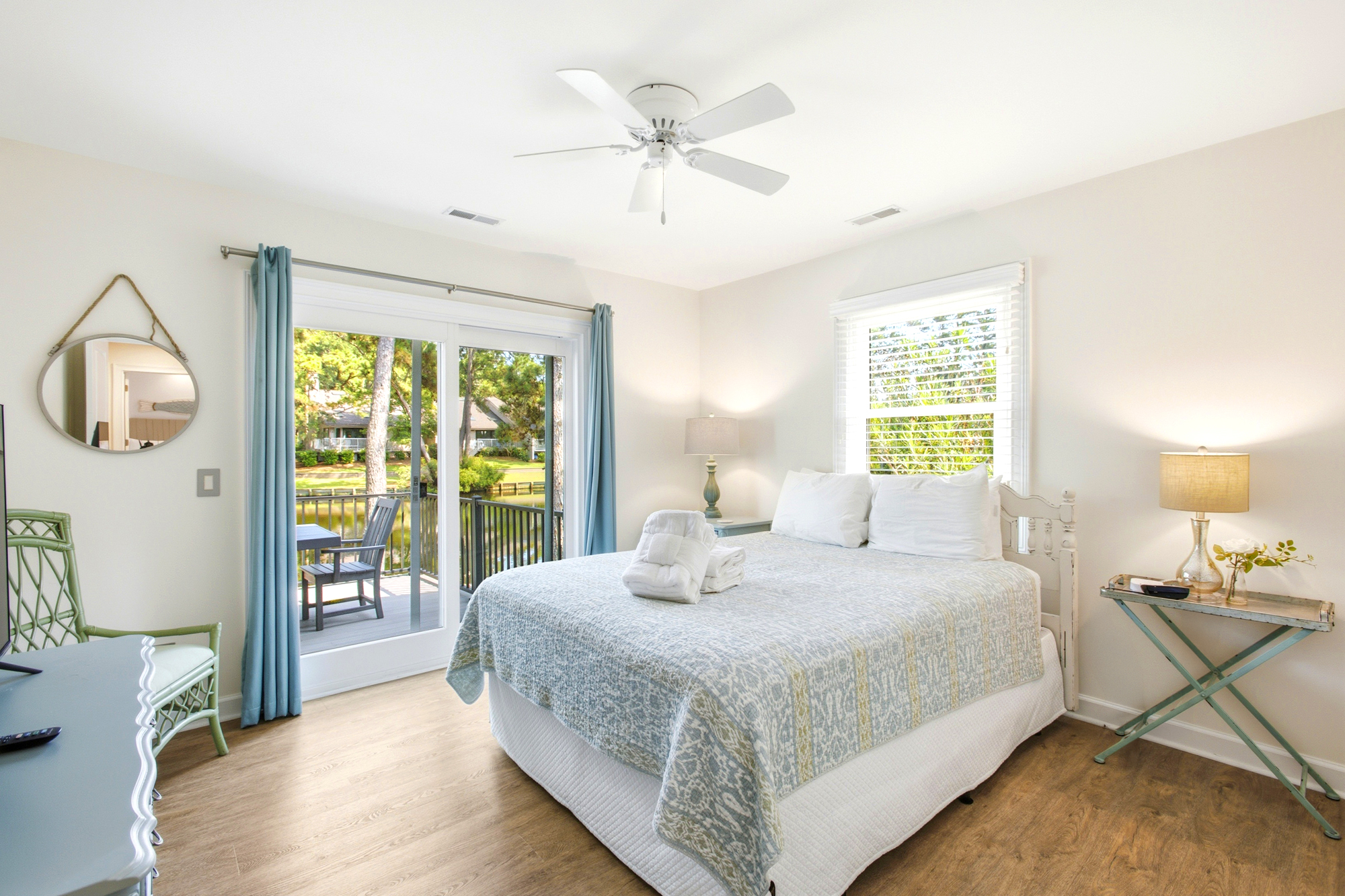 Pastel linens and airy blue curtains frame views of the water, creating a serene space for slow mornings. Sliding glass doors lead to a private balcony, letting in a gentle glow that warms the smooth wood floors.
