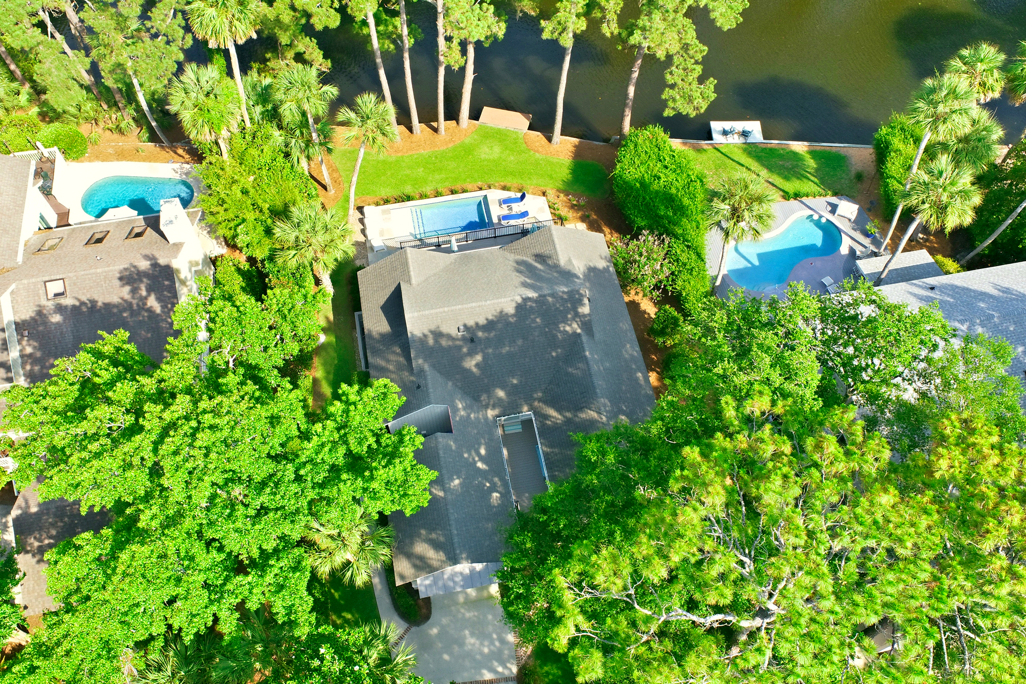 Emerald treetops frame this aerial view of your private poolside sanctuary, where turquoise waters meet the calm edge of a winding lagoon. Verdant lawns and swaying palms create a quiet, sun-drenched escape perfect for long afternoons outdoors.