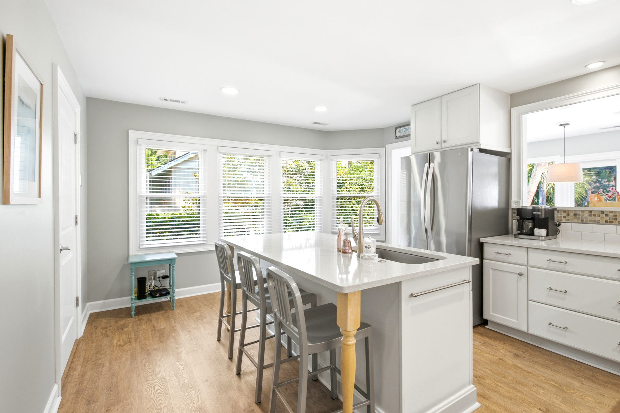 Polished quartz counters and stainless steel accents gleam in the soft morning glow of this airy kitchen. Wide windows invite the outdoors in, creating a bright and cheerful spot to gather for coffee at the central island.