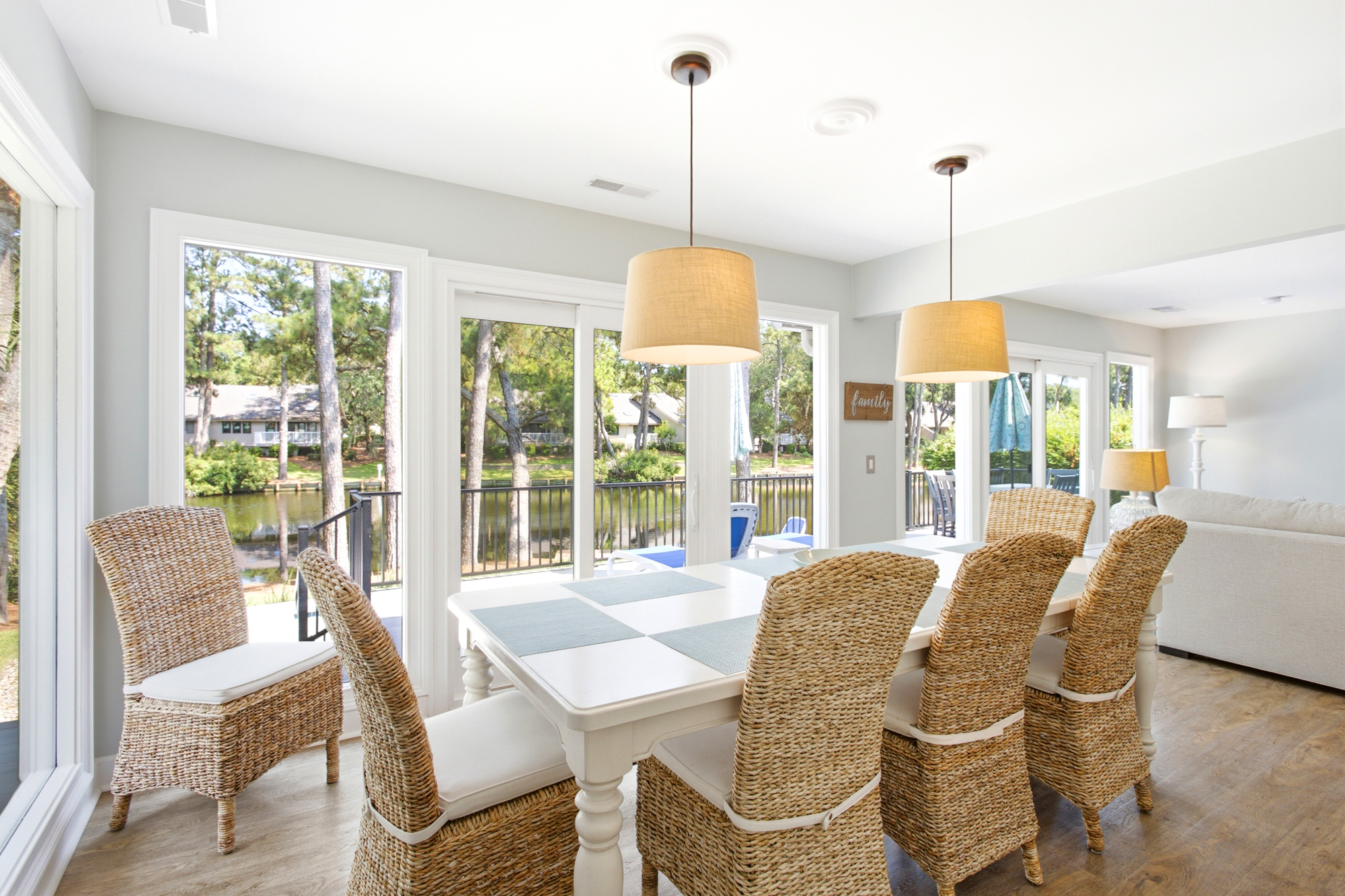 Woven textures and seafoam accents bring an organic warmth to this sunlit dining area. Floor to ceiling glass frames a peaceful waterfront view, creating a serene backdrop for shared morning coffee and slow afternoon meals.