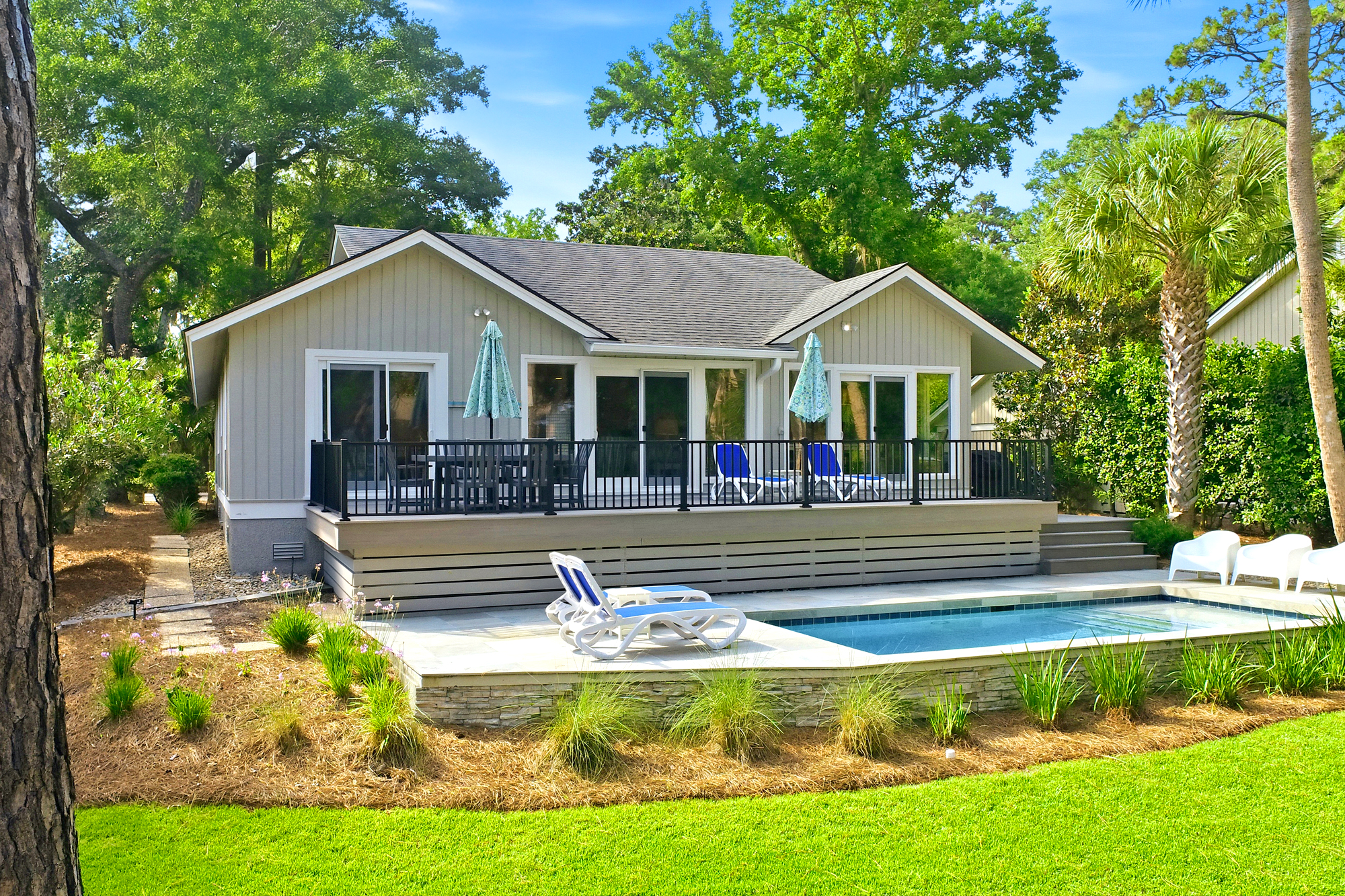 Turquoise waters glow beside a tiered wooden deck, offering a perfect spot for afternoon swims and outdoor dining. Towering oaks and palms frame this quiet backyard, where stone accents and lush lawns create a peaceful, sun-washed getaway.