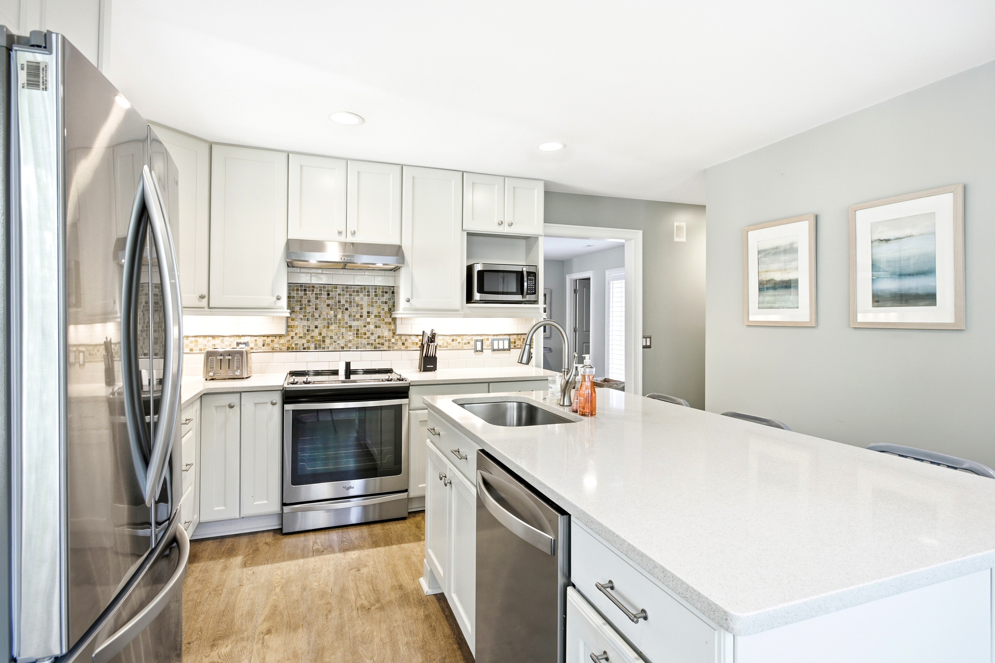 White cabinetry and sleek quartz counters create a bright, airy culinary space anchored by warm wood flooring. Modern stainless appliances and a textured tile backsplash add a touch of sophistication for your morning coffee or evening meal.