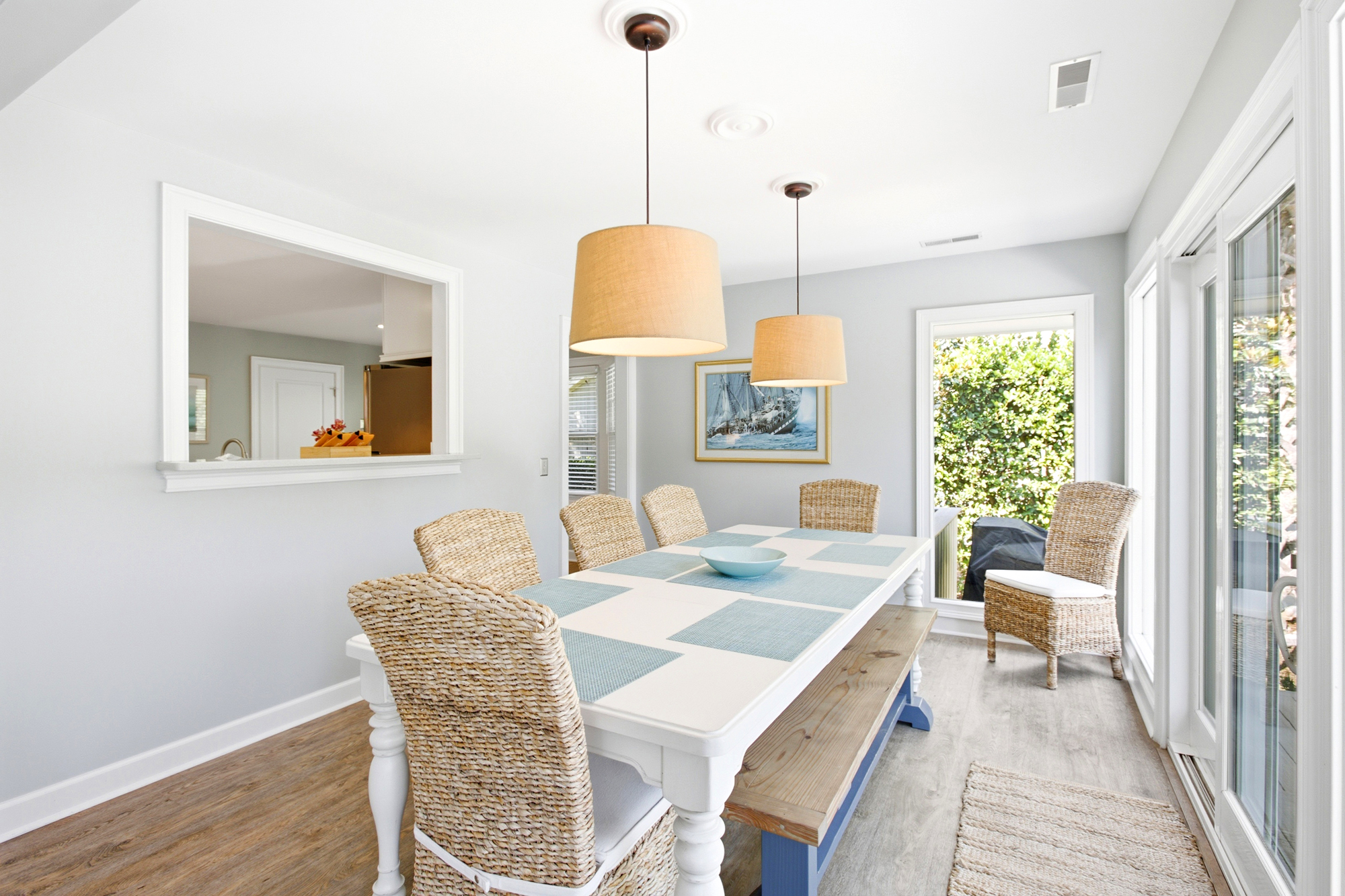 Natural seagrass chairs and a sturdy wooden bench surround this bright dining table, creating an airy spot for long brunches. Soft pendant lamps cast a gentle glow over the room while sliding glass doors pull in the lush garden views.