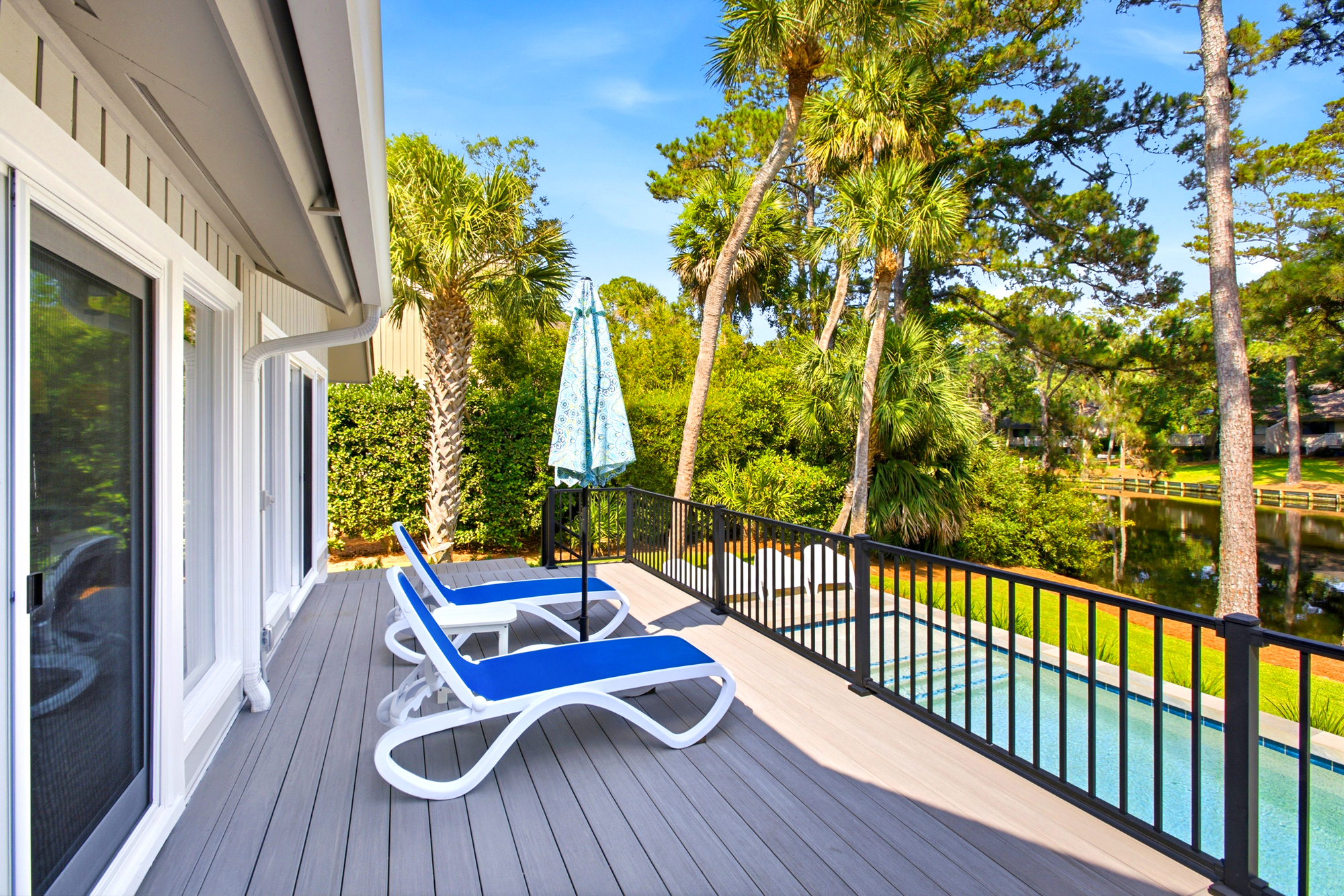 Azure loungers sit atop a smooth, sun-washed deck overlooking a private pool and a lush canopy of palms. The midday glow illuminates the water nearby, creating a serene spot to enjoy the quiet reflection of the lake.