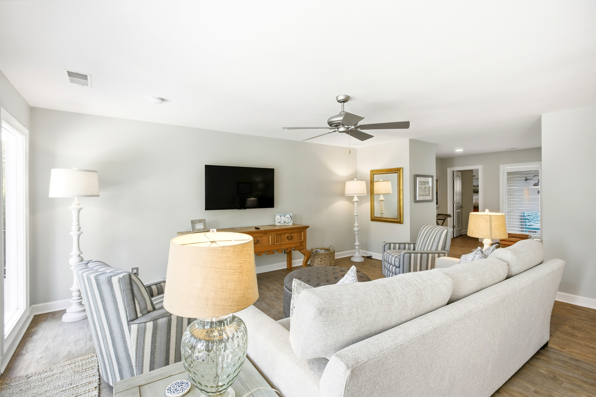 Soft linens and striped upholstery create a serene atmosphere for a quiet evening in. Warm lamp glow dances across rich wood textures and pale walls, offering a peaceful, airy lounge tailored for effortless conversation.