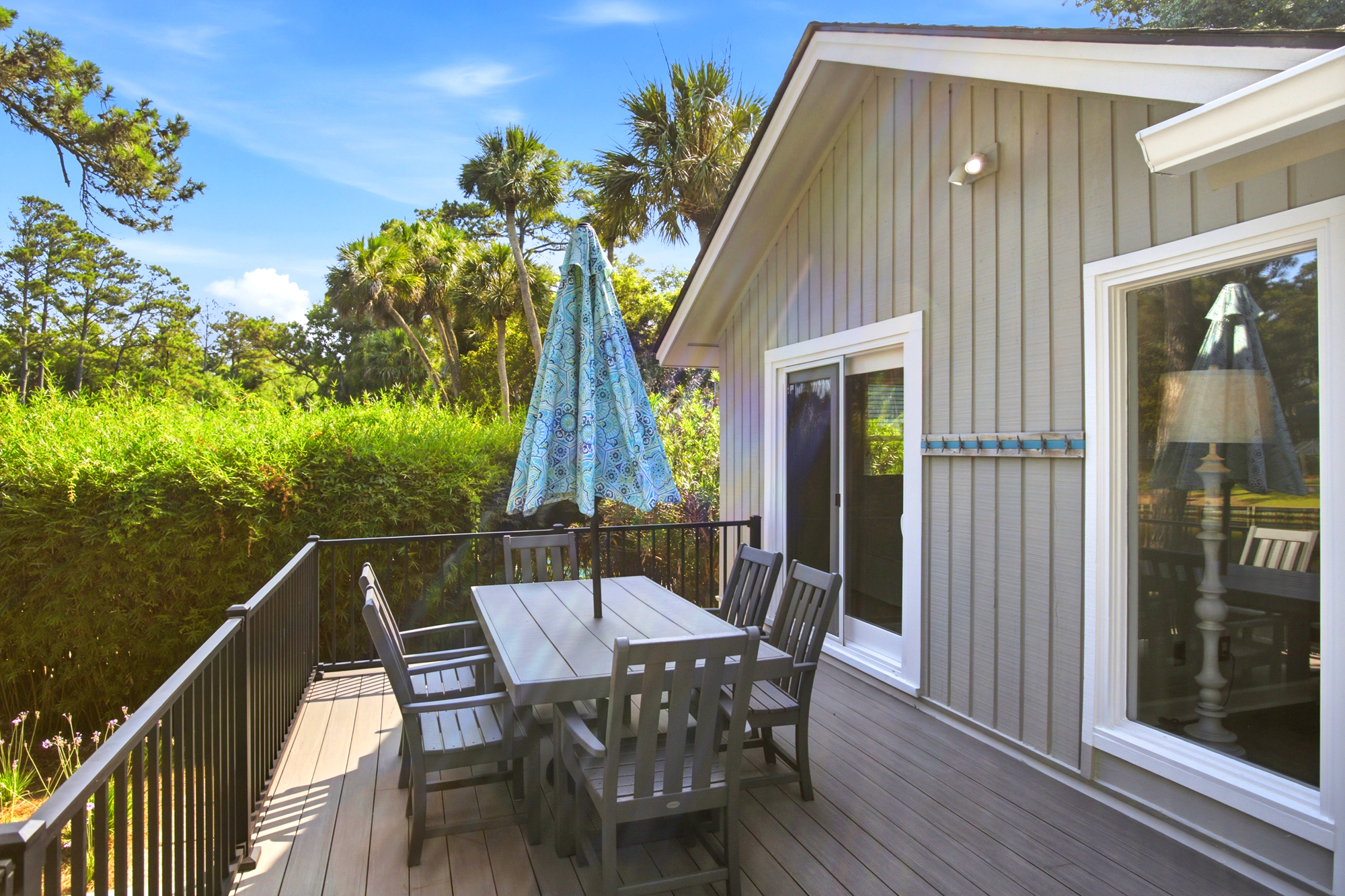 Fresh air and tropical palms frame this elevated deck, where a patterned umbrella shades the perfect spot for morning coffee. A sleek dining table offers a quiet perch to watch the golden hour glow dance across the lush garden greenery.