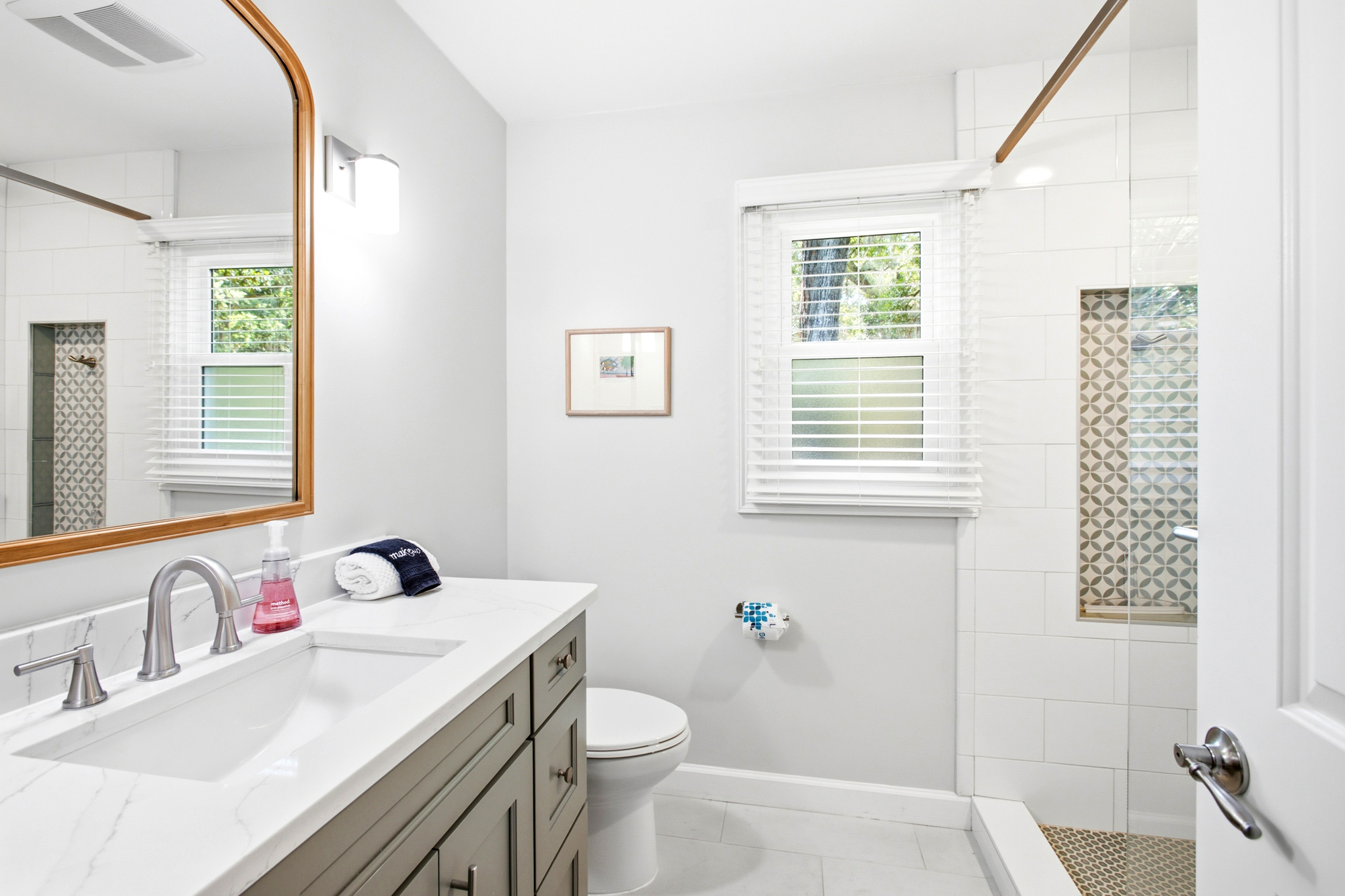 Alabaster walls and subway tiles glow under a wash of afternoon brightness, creating a calm space for your morning routine. Geometric patterns and warm wood accents ground this airy bathroom in quiet, clean style.