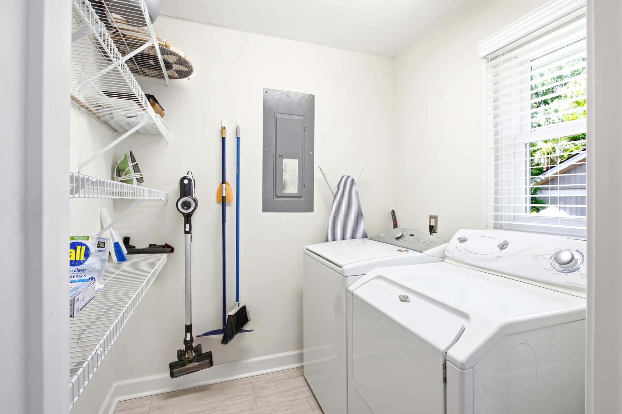Modern laundry facilities wait in a bright, organized nook where natural light filters through the blinds. Tidy wire shelving and essential cleaning tools ensure a smooth, worry-free stay for your longer adventures.
