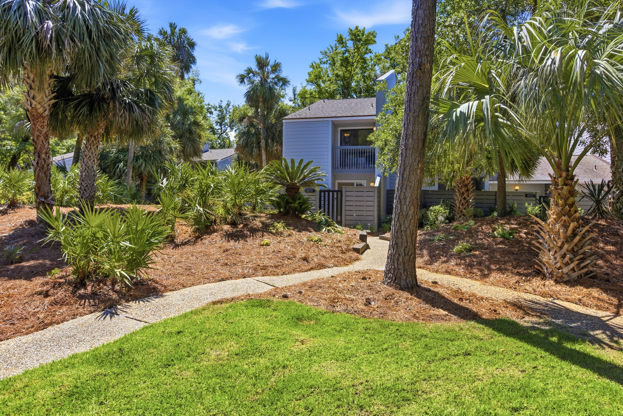 Palm-lined paths wind through vibrant greenery and soft pine straw, leading you home to this quiet coastal villa. Bright blue skies and swaying fronds create a serene, breezy atmosphere for your stay.