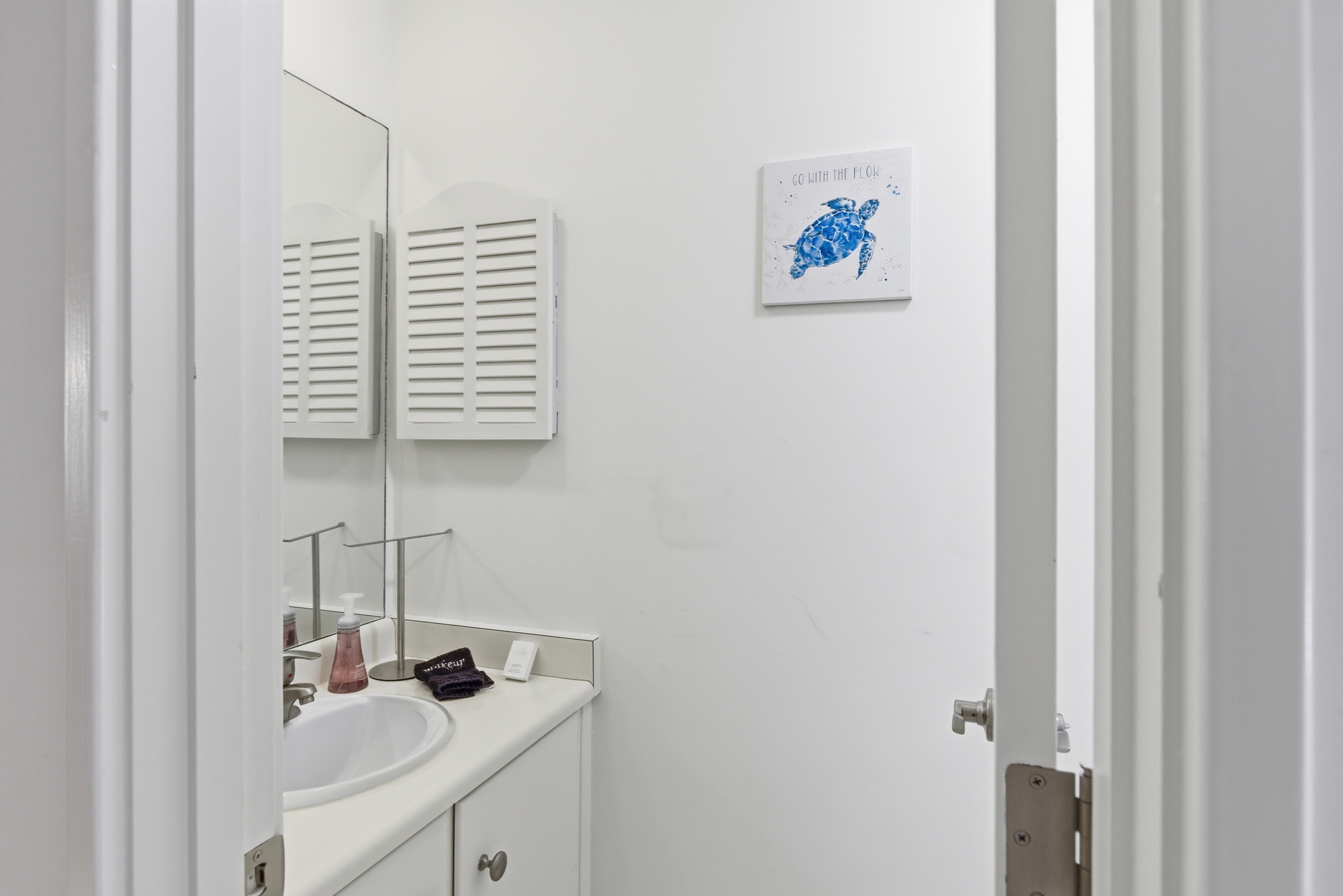 Coastal charm meets clean design in this airy bathroom, featuring a whimsical sea turtle print and crisp shutter details. Soft textures and bright surfaces create a refreshing space to prepare for your day at the beach.