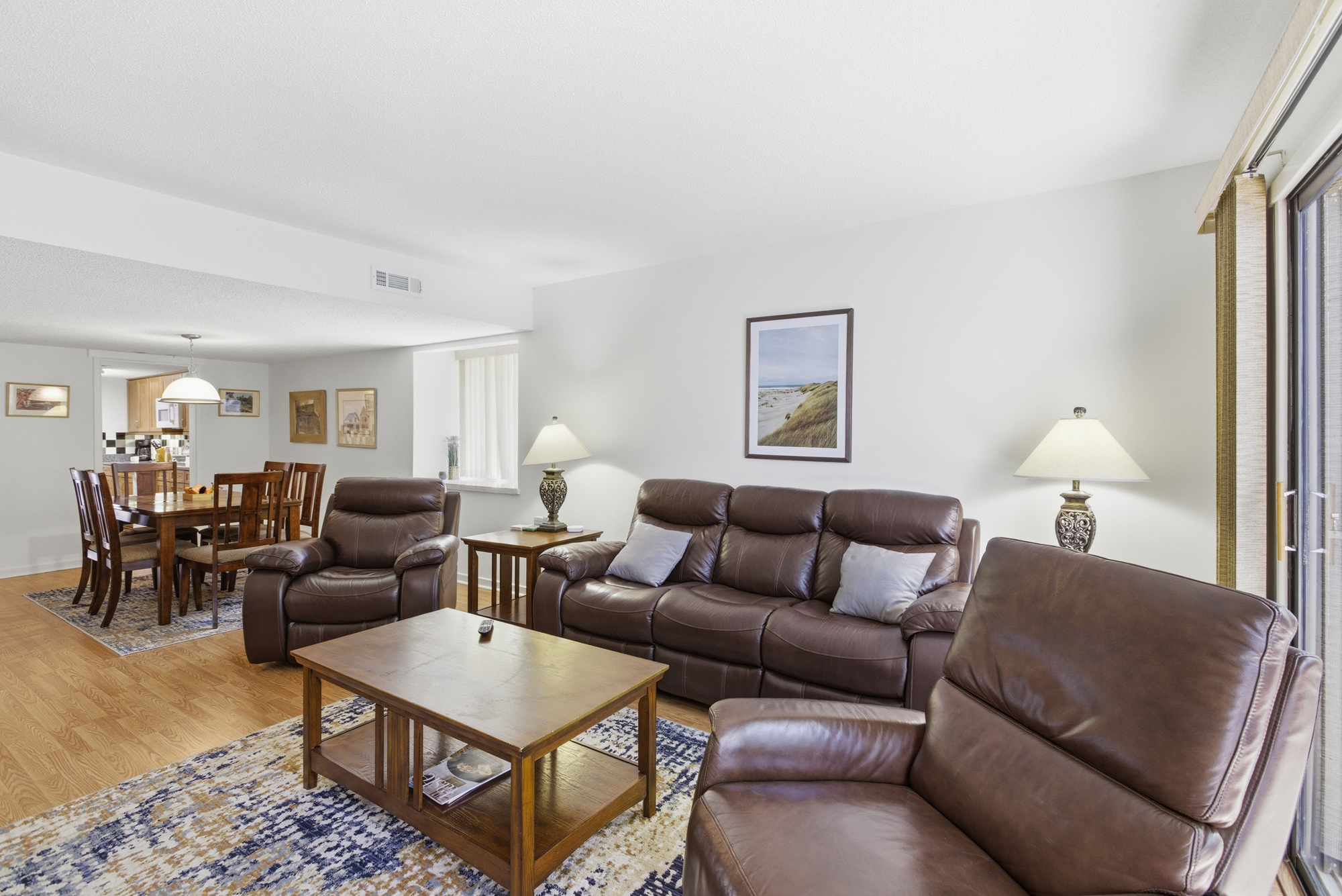 Leather seating anchors this airy living room, where golden afternoon glow streams through the glass door. Smooth wood textures and soft lamp light create a cozy atmosphere for quiet evenings and slow mornings.