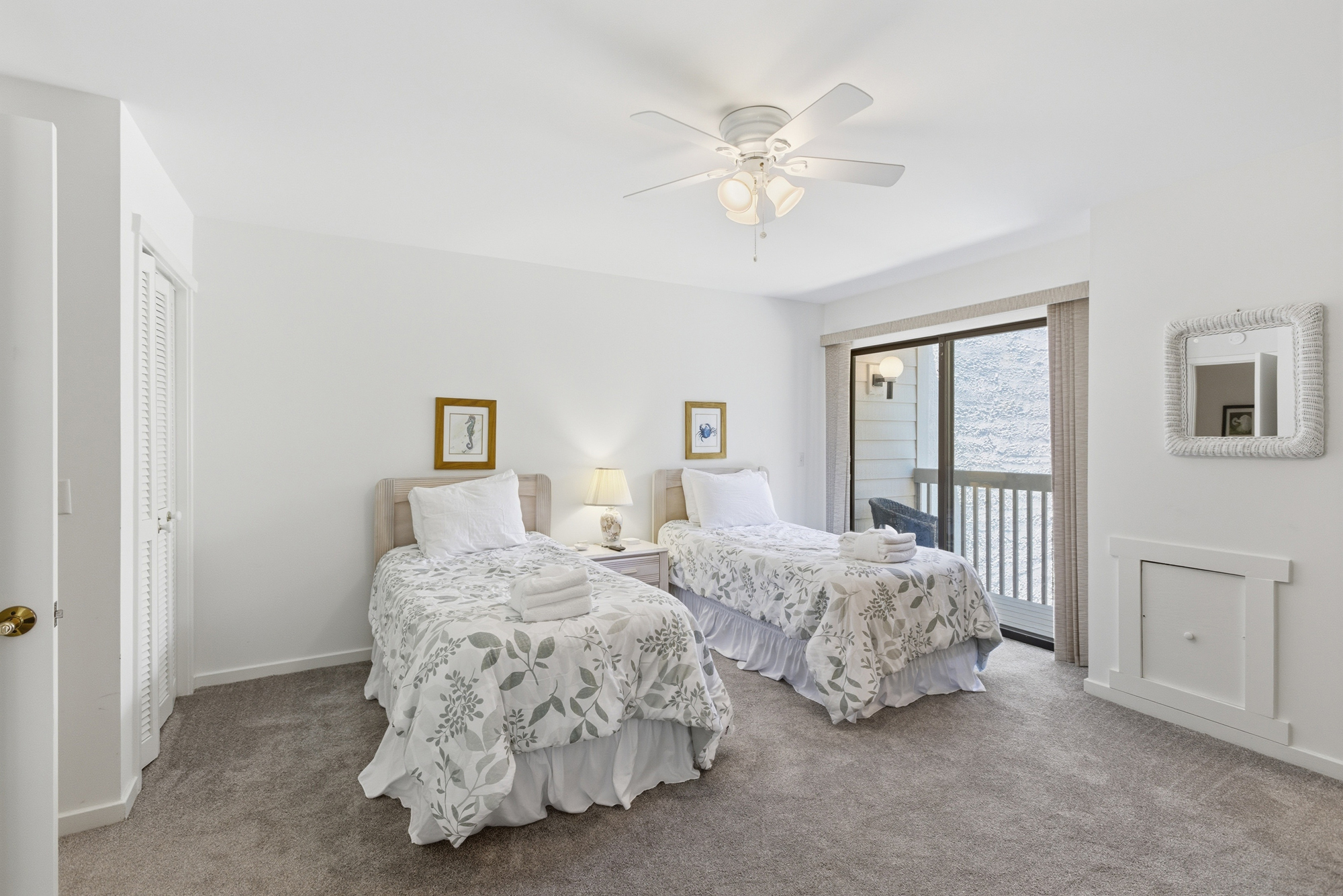 Twin beds dressed in crisp, botanical linens offer a serene spot to rest after a day at the beach. Glass doors lead to a private balcony, filling the airy room with soft afternoon light and a gentle coastal breeze.
