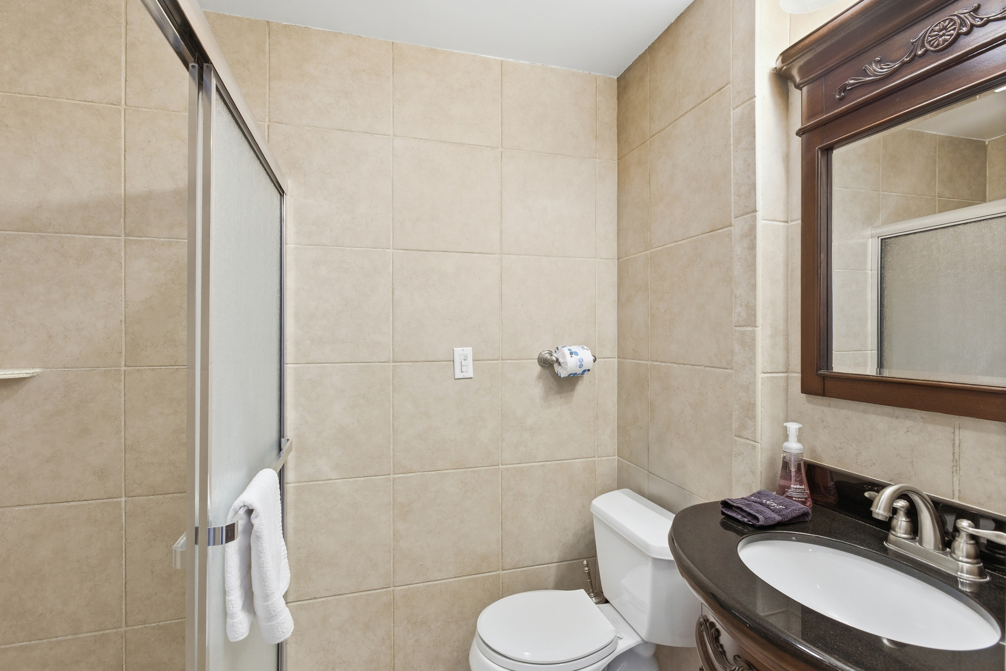 Earthy stone tiles wrap this quiet bathroom in soothing, neutral tones. A dark granite vanity and ornate wood mirror add a touch of timeless elegance, creating a clean and functional space for your morning routine.