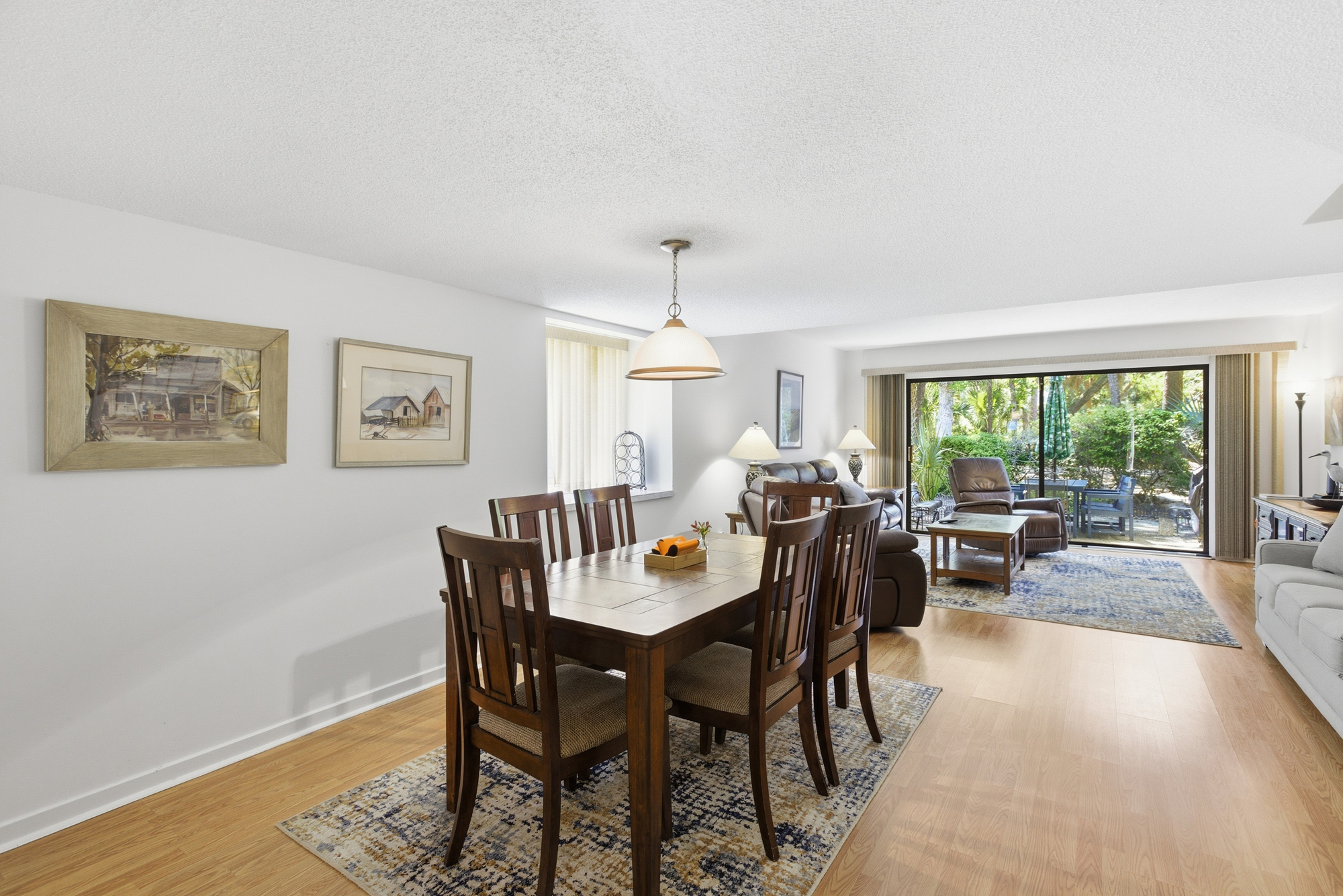 Polished timber floors and a sturdy oak dining set anchor this airy room, where soft daytime brightness flows in from the patio. Plush seating and coastal artwork create a calm, grounded atmosphere perfect for shared meals and easy conversation.