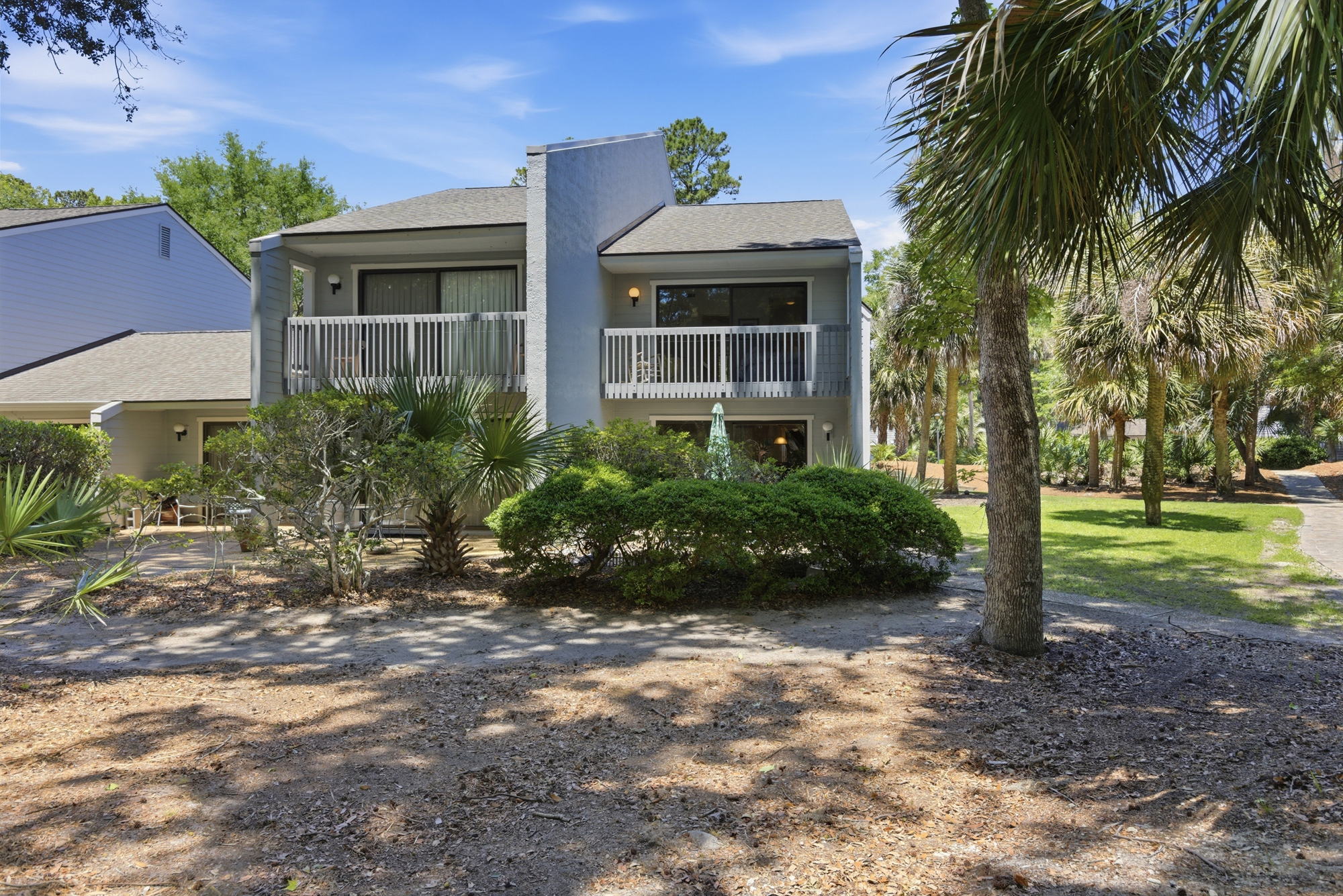 Morning shadows stretch across the sandy path leading to this serene villa, where private balconies overlook a lush garden of tropical greenery. Soft grey siding and clean lines create a peaceful backdrop for your peaceful island getaway.