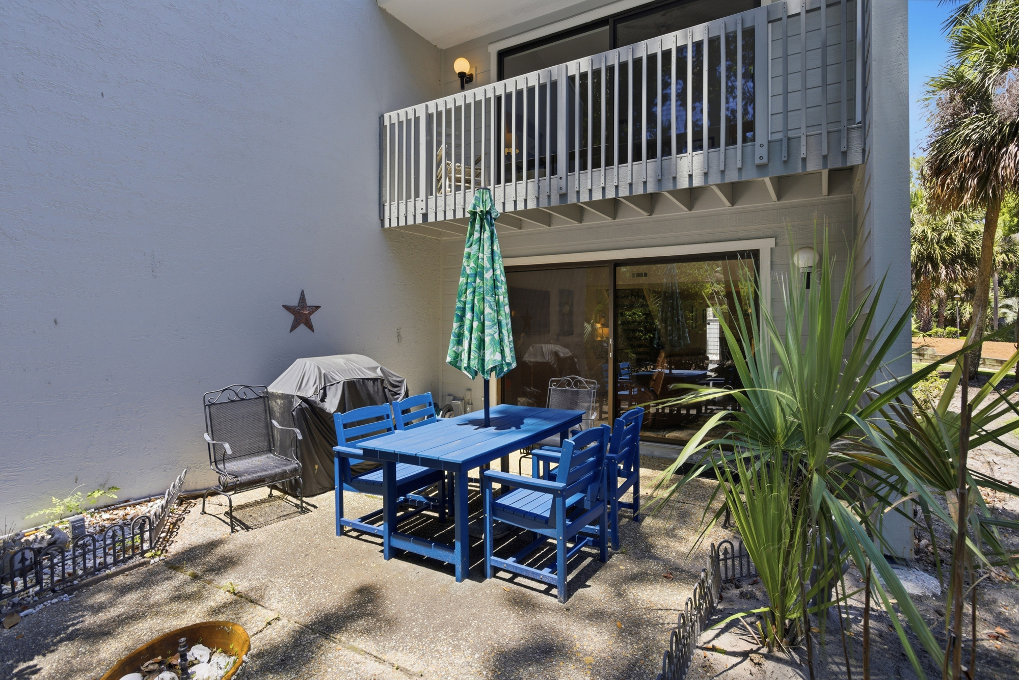 Vibrant blue wooden furniture anchors this private stone courtyard, offering a cheerful spot for alfresco meals under the dappled shade. Tropical greenery and a nearby grill create an effortless setting for slow, sunlit afternoons outdoors.