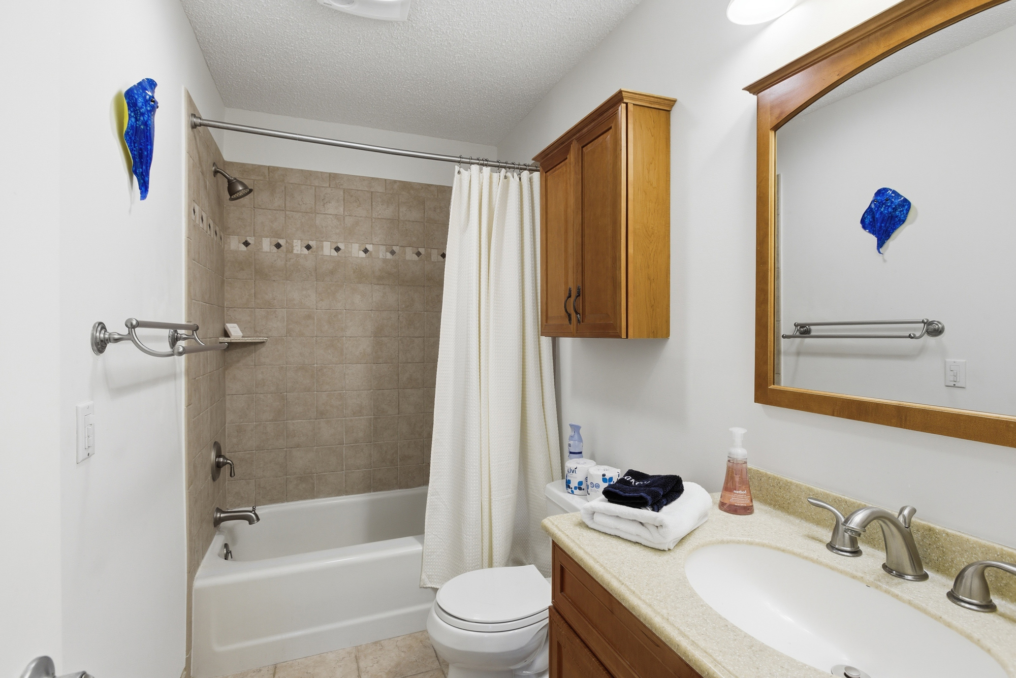 Warm wood cabinetry and earth-toned tiles provide a grounded, serene atmosphere for your morning routine. Cobalt blue accents pop against the clean, bright walls, while plush towels wait by the vanity for a refreshing start to the day.