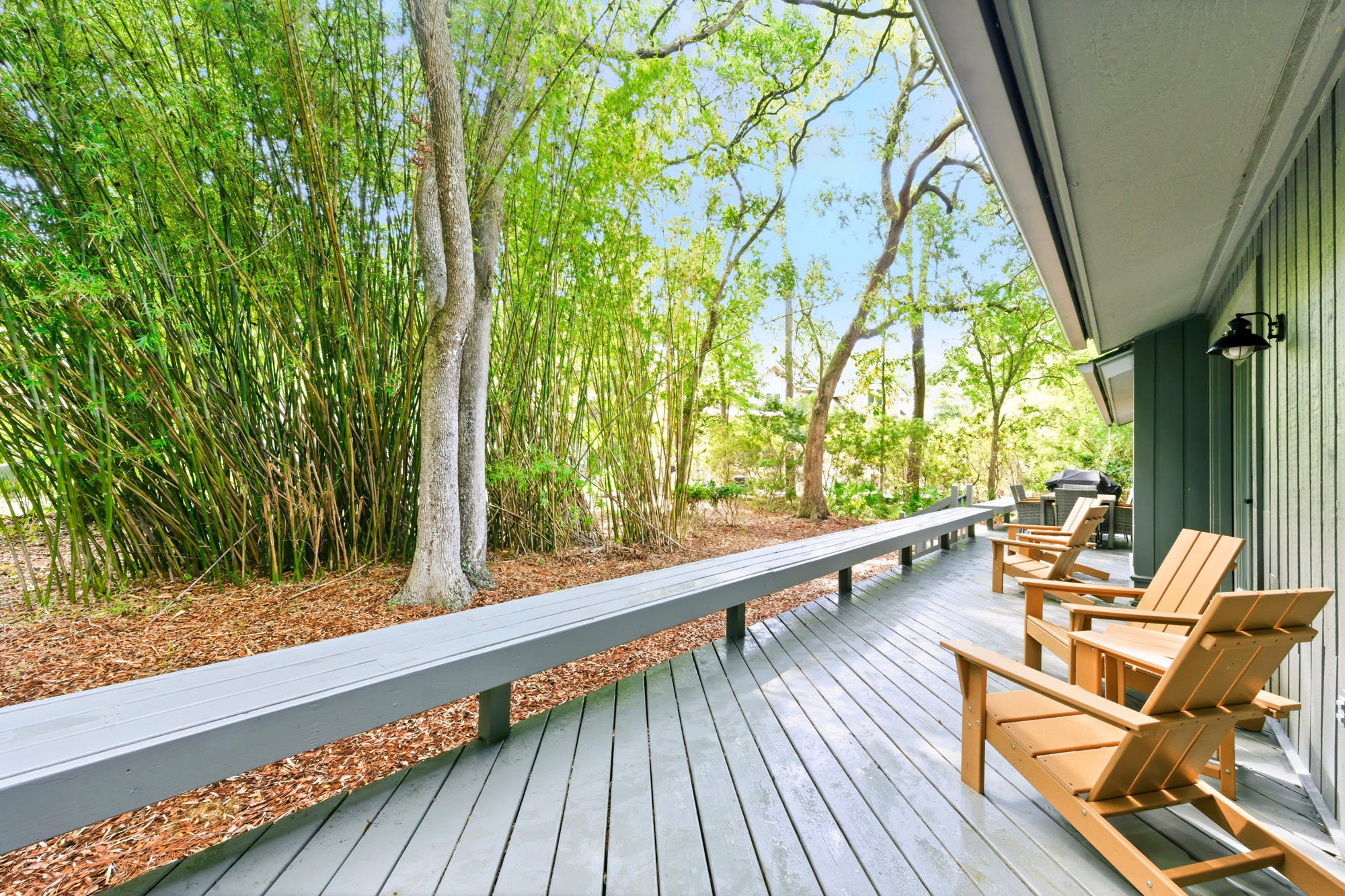 Spanish moss trees sway gently beside this expansive gray deck, where warm cedar chairs invite slow mornings in the fresh air. The surrounding canopy filters the bright sky, creating a calm and secluded outdoor living space for quiet reflection.