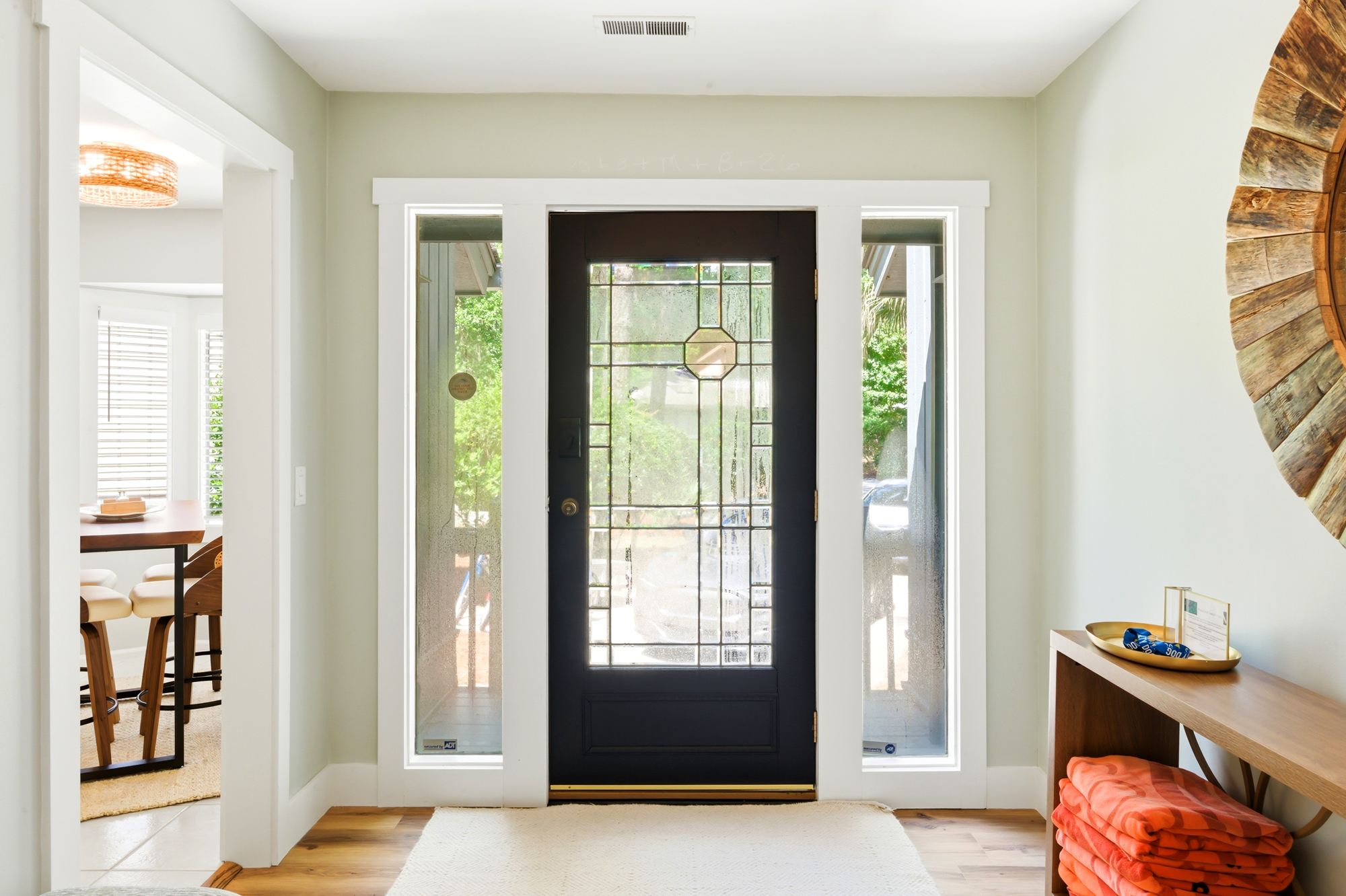 Leaded glass panels and a bold dark door frame the entry, filtering soft daylight onto the oak floors. This airy foyer pairs sculptural wood accents with a clean, modern aesthetic to offer a calm and sophisticated greeting.