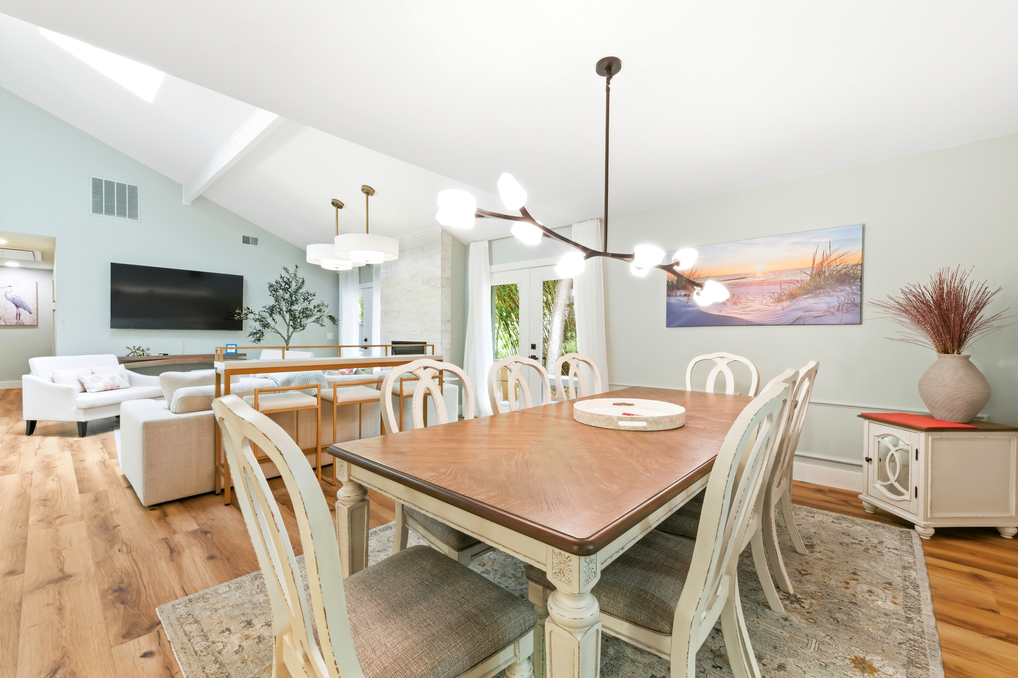 Polished oak and carved cream chairs anchor this airy dining space, where a modern branch chandelier glows overhead. Vaulted ceilings and soft sage walls create a calm, open atmosphere for shared meals and morning coffee.
