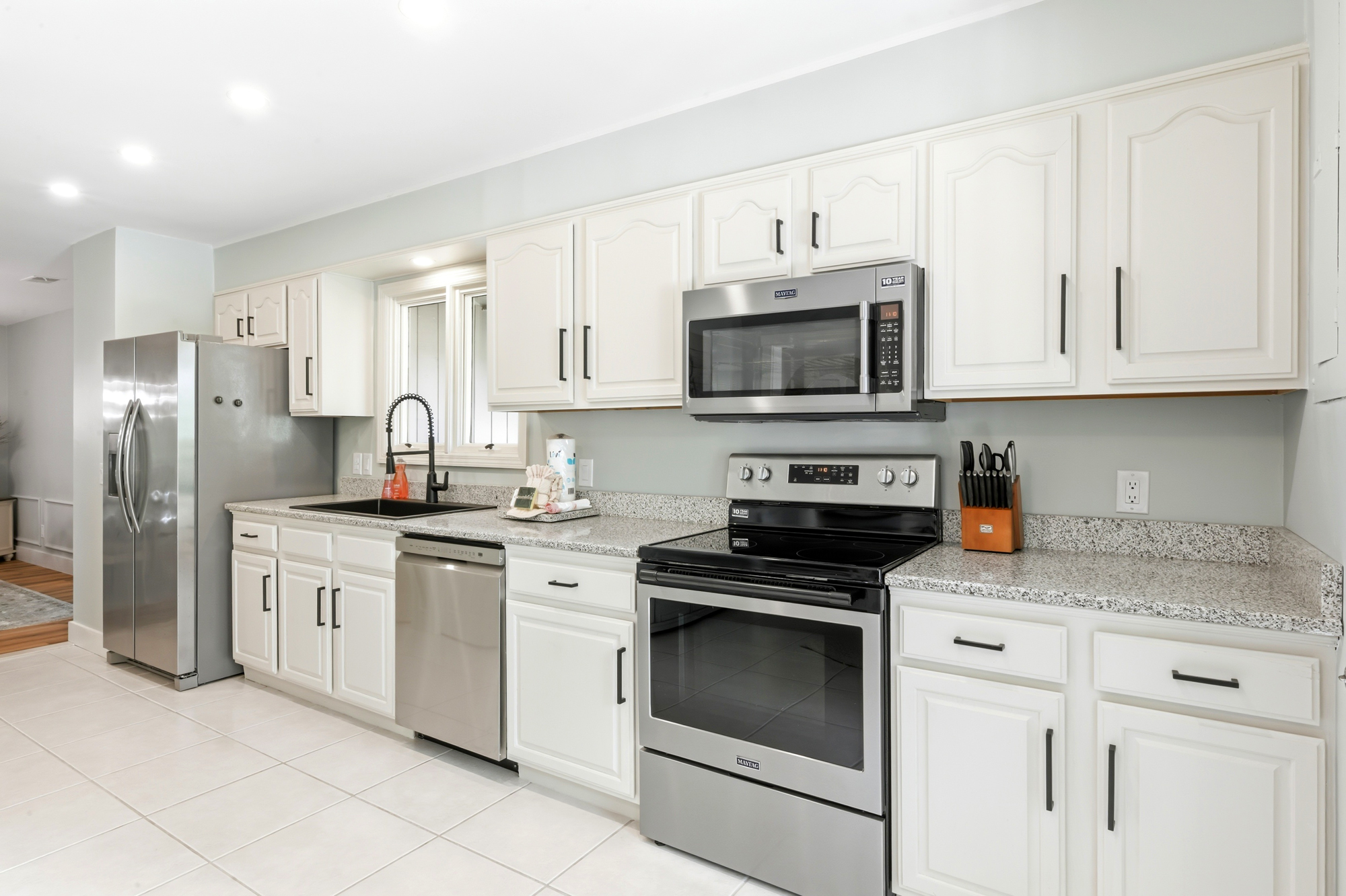 Creamy white cabinetry and speckled stone surfaces create a tidy, luminous workspace for your morning coffee. Modern stainless appliances shimmer under soft recessed lighting, offering a sleek yet homey atmosphere for every meal.