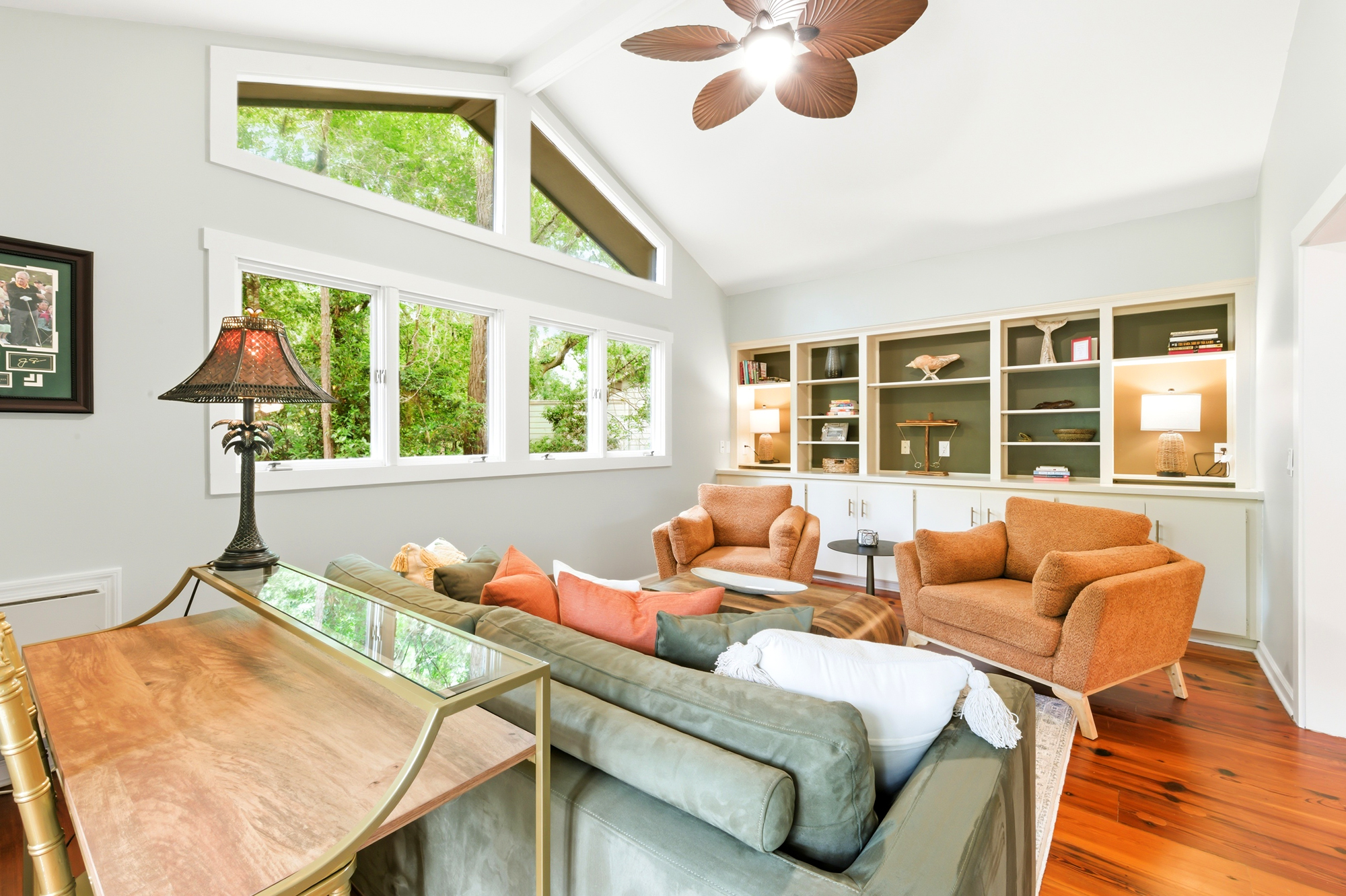 Soaring ceilings and expansive windows pull the lush greenery indoors, creating a serene backdrop for the earthy textures and plush seating. Warm wood floors anchor this airy living space, perfect for quiet afternoons or late night conversations.