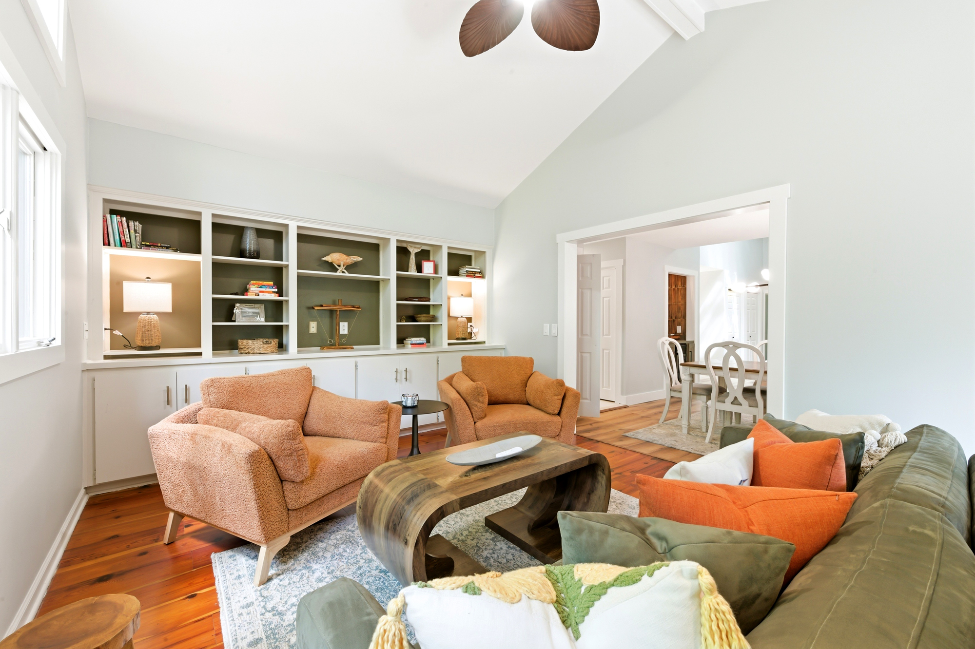 Terracotta armchairs and mossy velvet pillows bring a rich, earthy warmth to this airy living room. Sculptural wood furniture and built-in shelving create a curated, homey feel beneath the vaulted ceiling and soft afternoon glow.