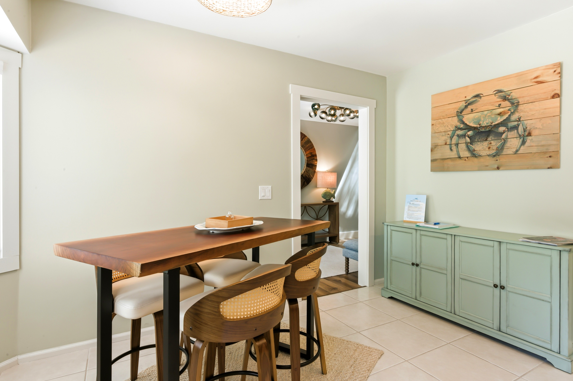 Smooth timber and coastal hues create a serene nook for morning coffee. This cozy dining corner features rattan-backed seating and sea-inspired art, bathed in a soft afternoon glow that invites quiet conversation.