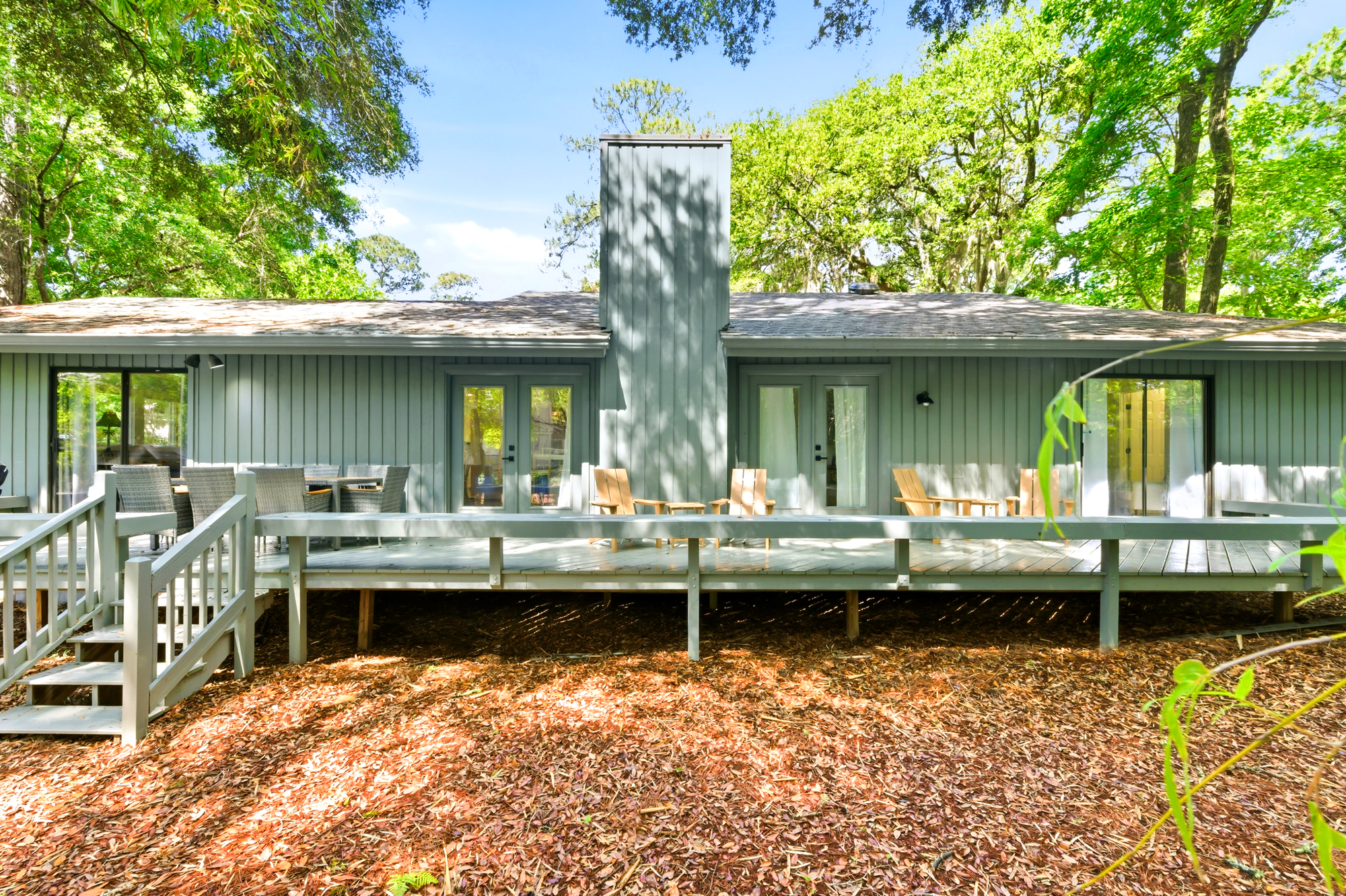 The backyard is a serene outdoor sanctuary under the dappled shade of majestic oaks. Afternoon glow illuminates the seating areas, offering a quiet spot to breathe in the forest air.