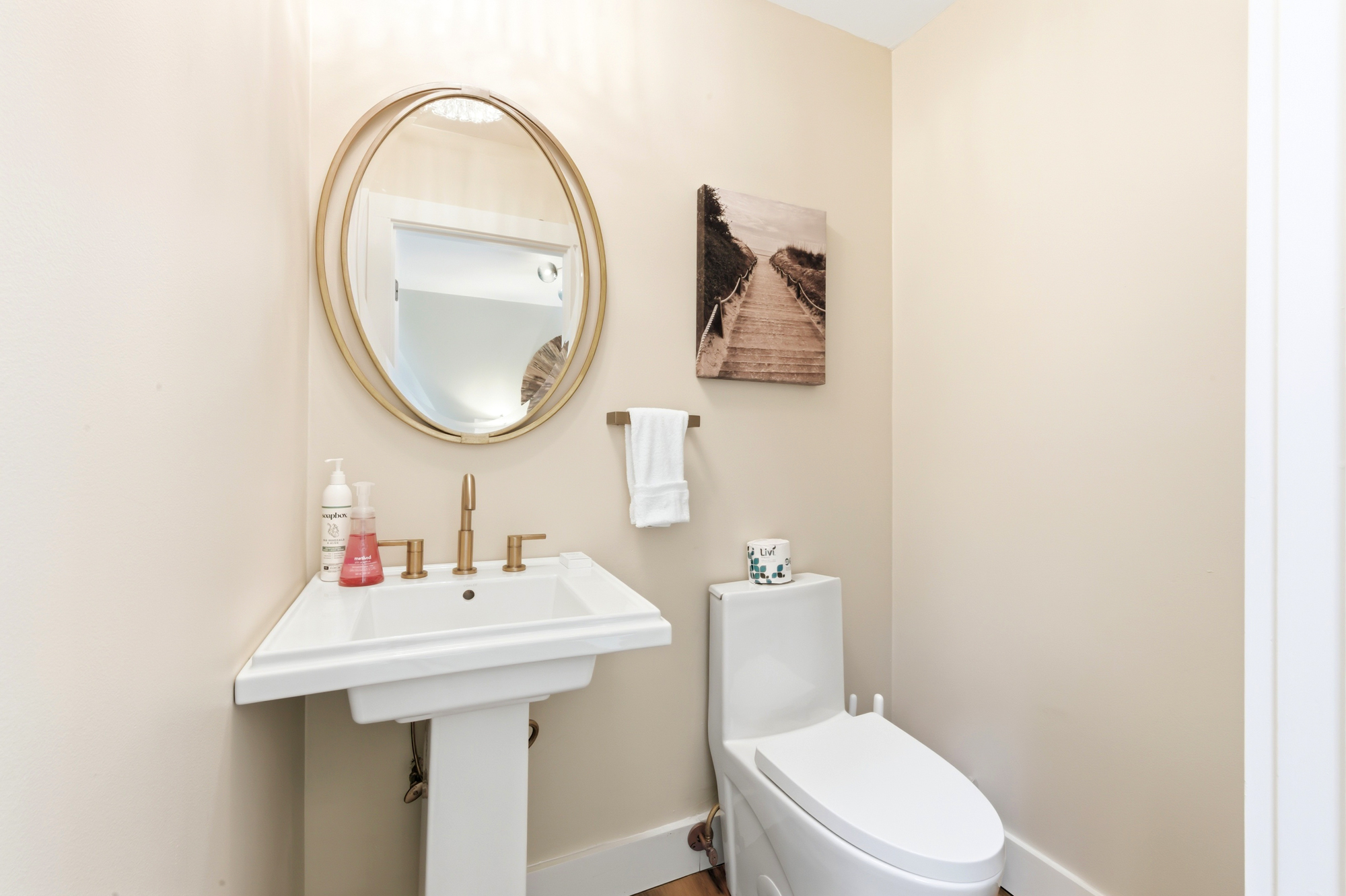 Gilded fixtures and a circular mirror add a touch of elegance to this calm powder room. Soft cream walls catch the gentle glow, creating a serene and tidy corner for a quick refresh.