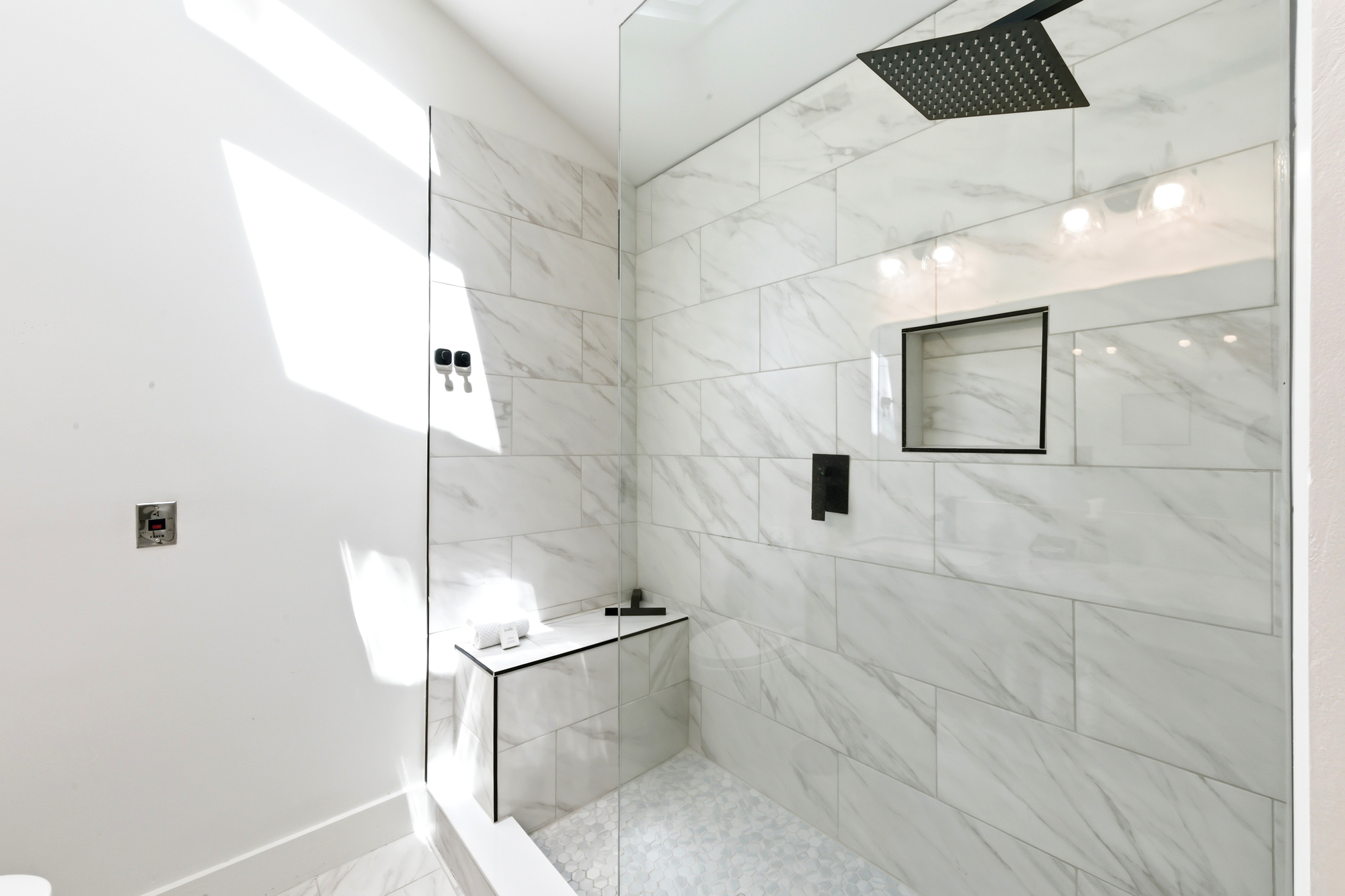 Veined tiles and matte black fixtures create a spa-like sanctuary where an afternoon glow dances across the glass. This sleek walk-in shower offers a peaceful start to your morning under a wide rainfall head.