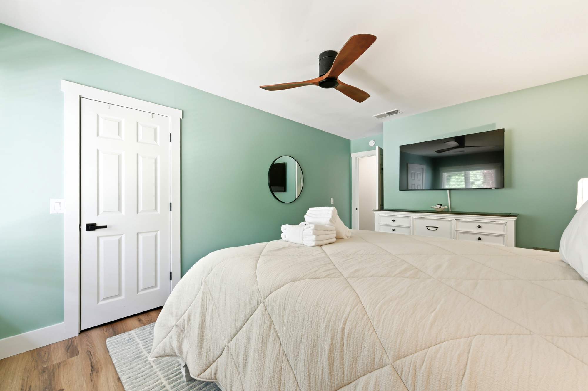 Seafoam walls and a carved wood ceiling fan create a serene backdrop for a quiet morning in bed. This airy suite offers a plush quilted duvet and organized white finishes, making for a tidy, tranquil corner to rest and recharge.