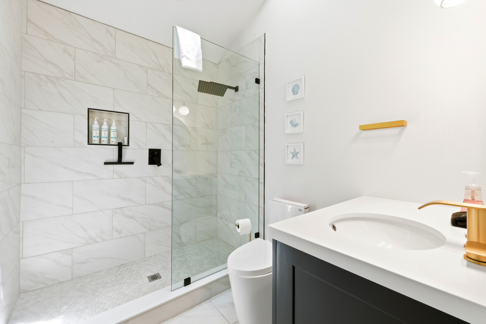 Gold fixtures add a touch of luxury to this modern bathroom, where clean lines and subway tiles create a refreshing spa atmosphere. Large glass doors open to a spacious shower, inviting you to start your morning in a bright, airy sanctuary.