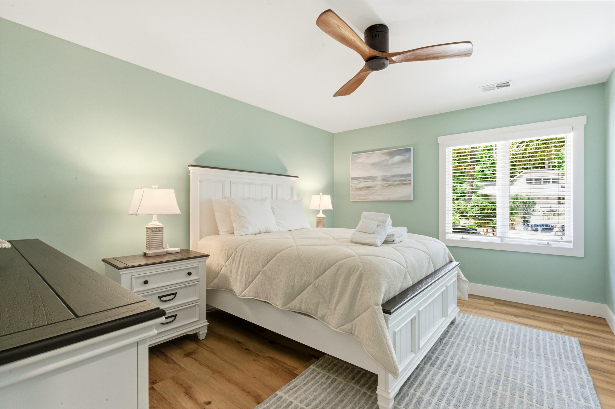 Sage walls and natural wood floors create a serene backdrop for this airy bedroom. A steady breeze from the timber fan complements the soft linens and dappled morning light, offering a peaceful sanctuary for your stay.