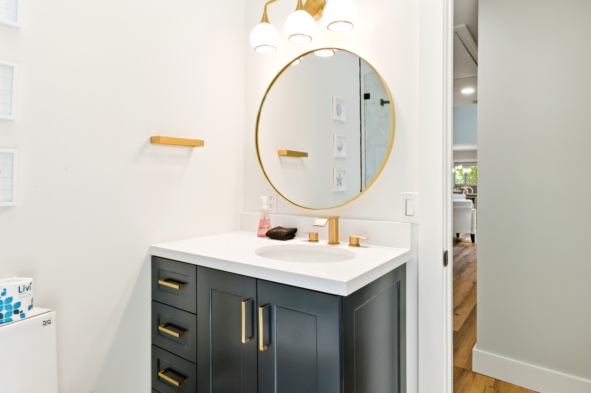 Golden accents shimmer against a charcoal vanity and snowy counters, creating a spa-like atmosphere for your morning routine. A circular mirror reflects the quiet, airy clean lines of this modern bathroom.