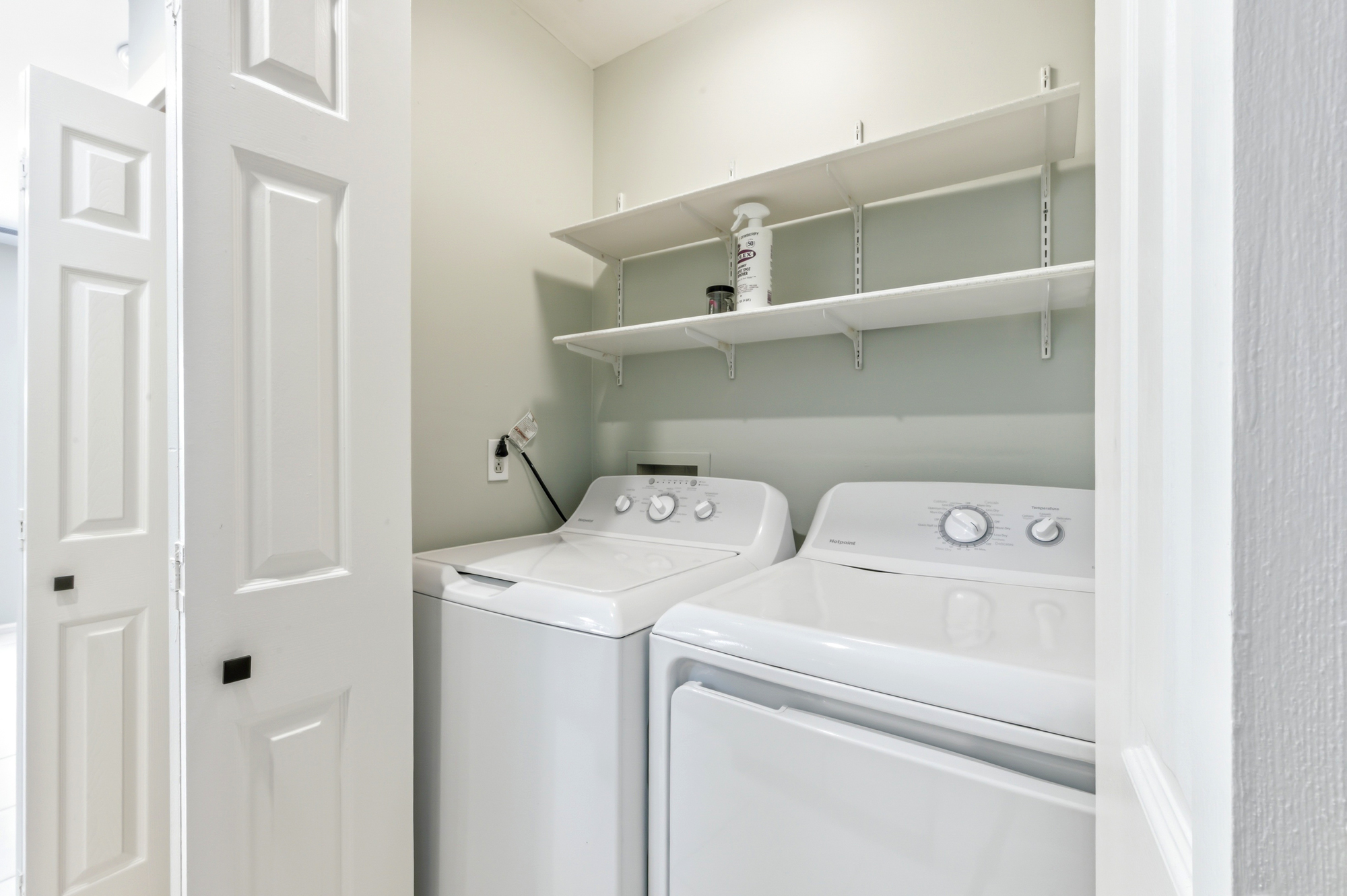 Fresh white appliances and organized shelving create a bright, functional laundry nook for your convenience. Soft sage walls and clean lines provide a calm atmosphere for managing your wardrobe during your stay.