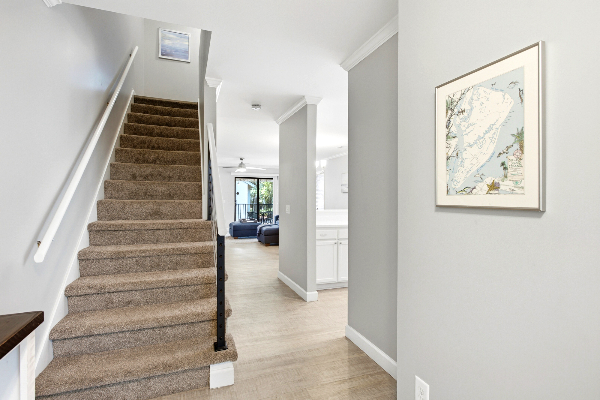 Soft plush carpeting meets crisp white trim in this bright entryway, leading your eye toward a sun-drenched living area. Minimalist coastal art and cool gray tones create a serene, airy atmosphere for a peaceful morning.