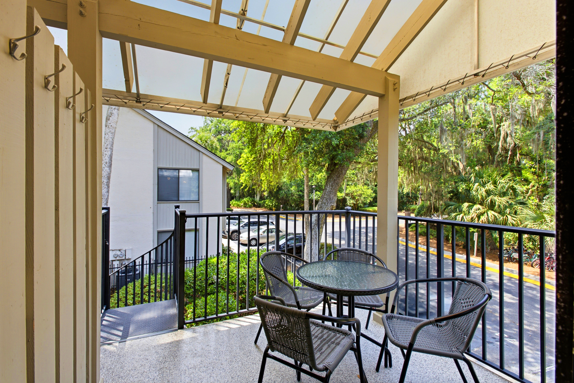 Woven chairs and a glass table wait on this covered balcony, where a canopy protects your morning coffee. Mossy trees and golden afternoon rays create a peaceful backdrop for outdoor dining over the quiet view.